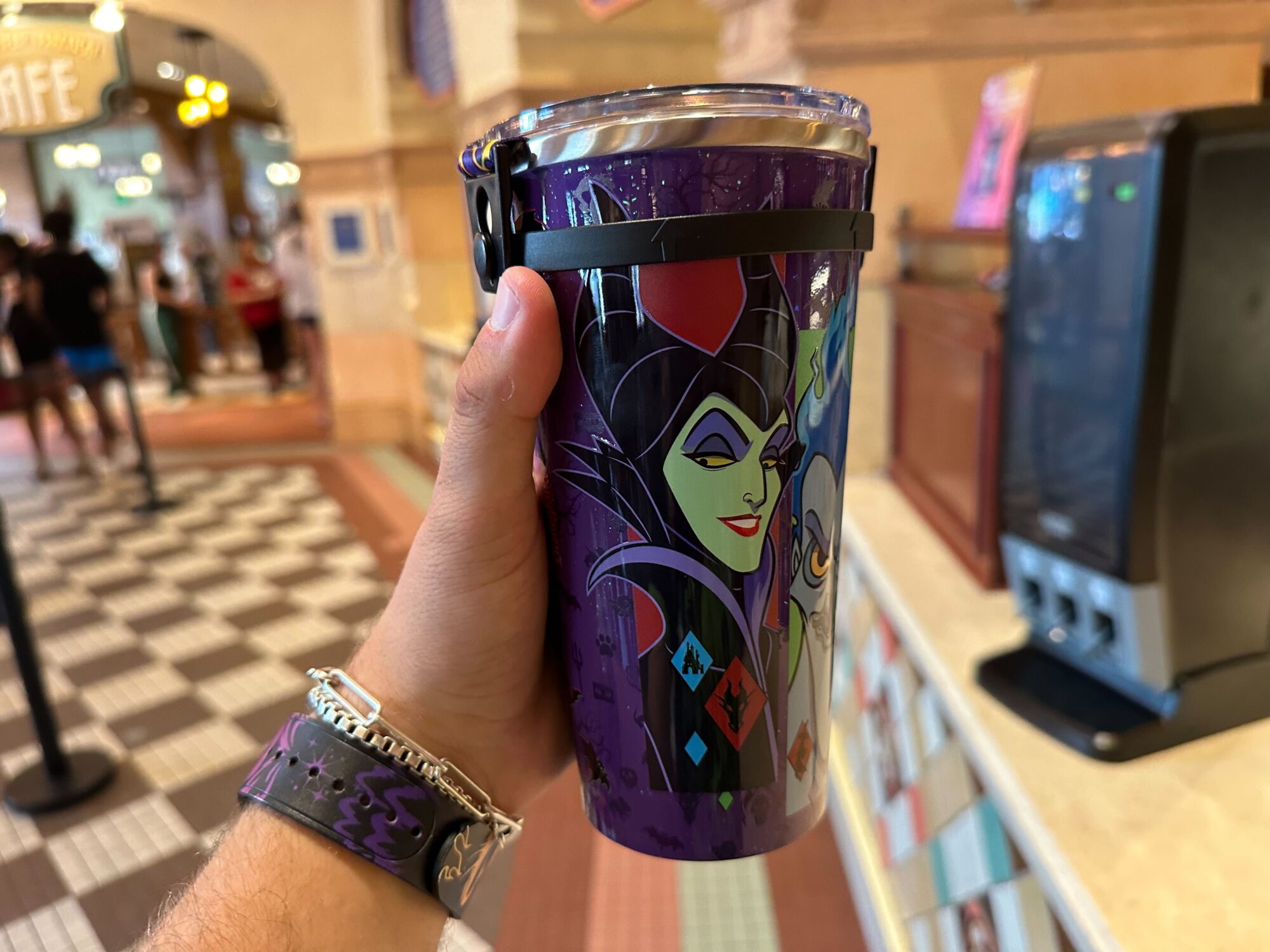 A person holds a purple tumbler featuring a design with the characters Maleficent and Ursula.