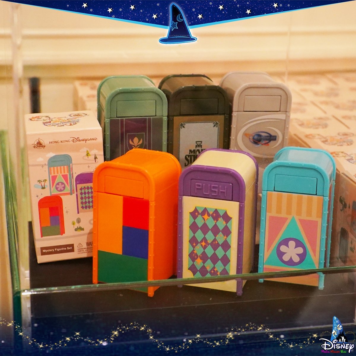A display of colorful collectible park trash can figurines from Hong Kong Disneyland, featuring various designs and patterns, is showcased behind glass with a Disney logo in the corner.