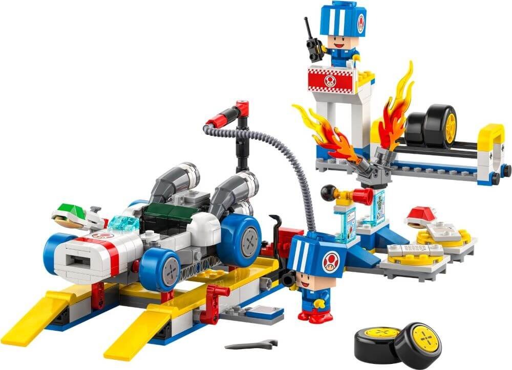 A LEGO set featuring a race car in a garage setting with a mechanic, pit crew members, and Super Mario-themed elements. The scene includes a tool station, fire elements, and spare tires.