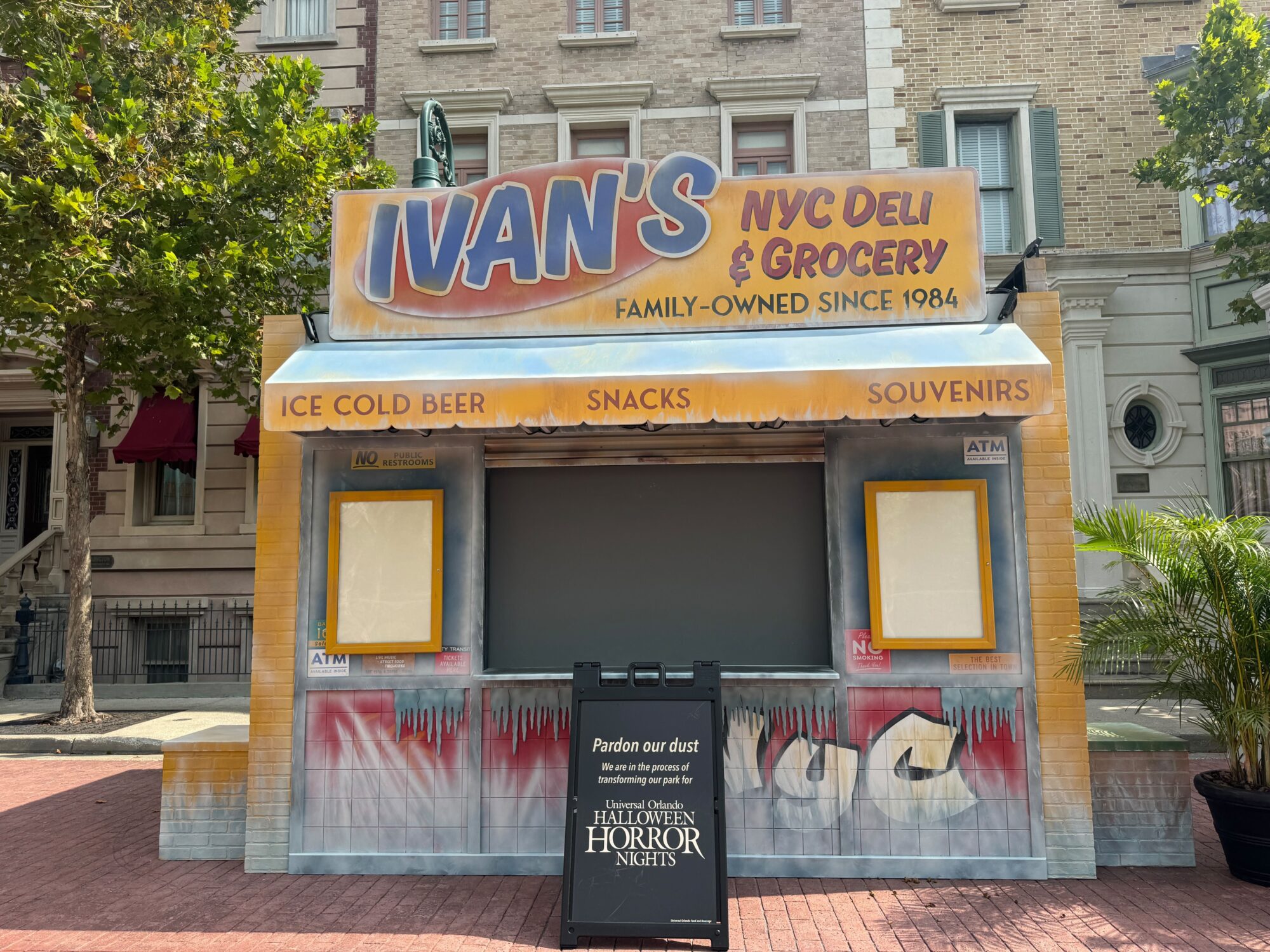 Closed food stand named "Ivan's NYC Deli & Grocery" with a signboard in front mentioning "Halloween Horror Nights" and asking visitors to pardon the construction dust as they transform the area into a thrilling scare zone.