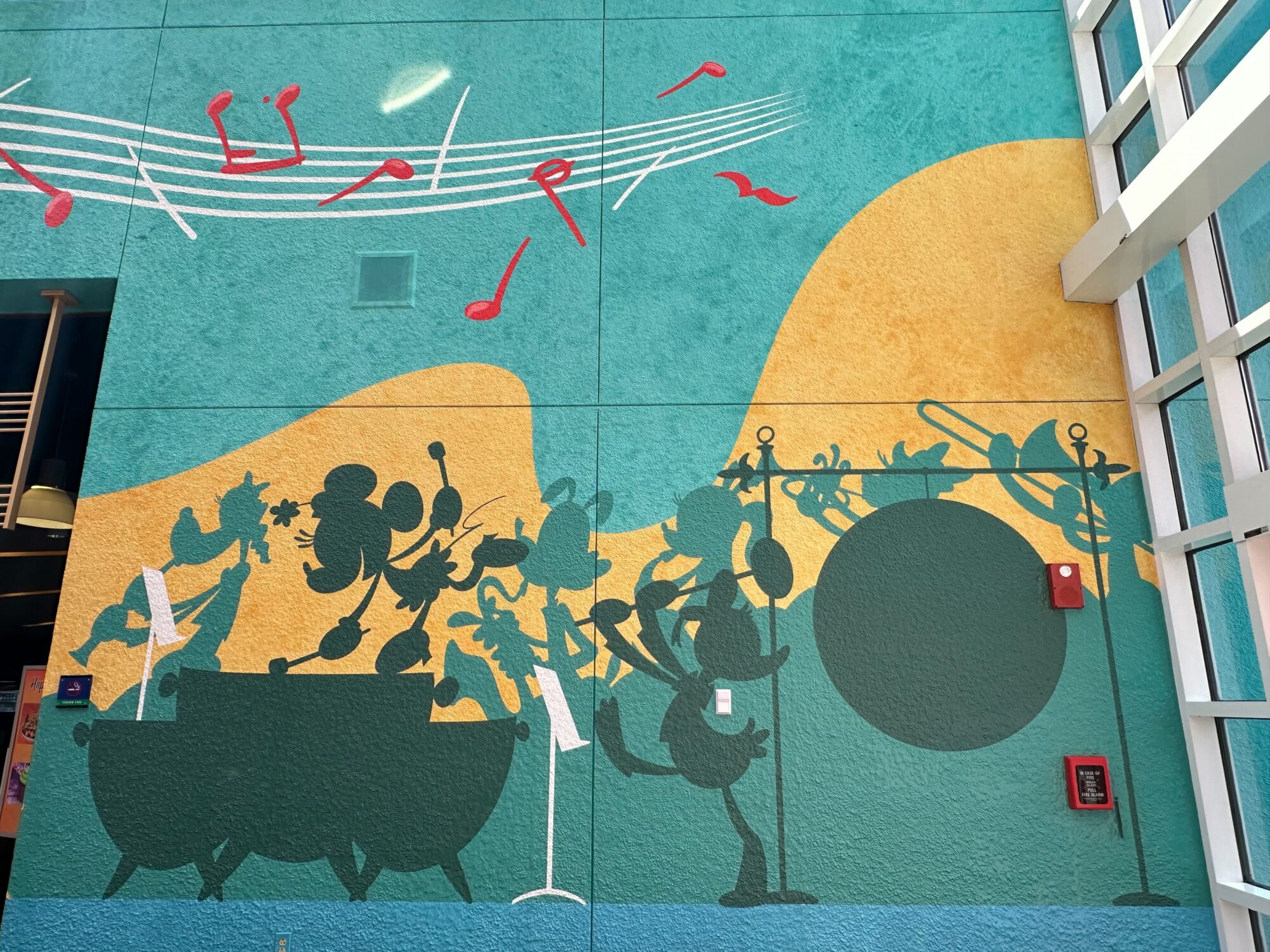 A colorful mural features silhouettes of Disney characters playing musical instruments on a teal and yellow background, with musical notes above them.