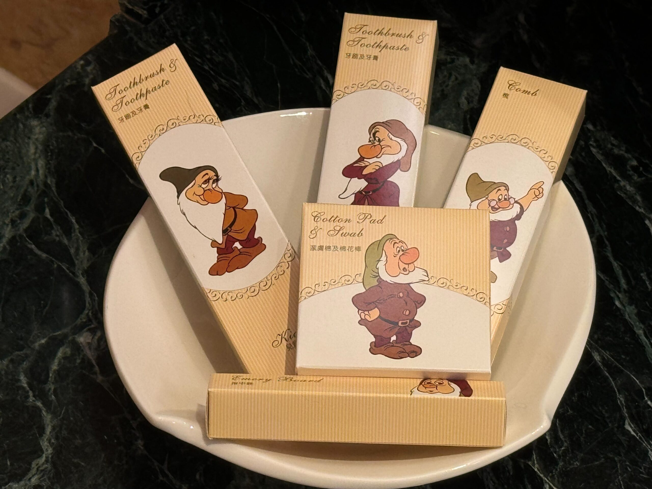 Bathroom set with toothbrush, toothpaste, comb, and cotton pads displaying cartoon dwarf illustrations placed in a white bowl from the Deluxe Room at Hong Kong Disneyland Hotel.