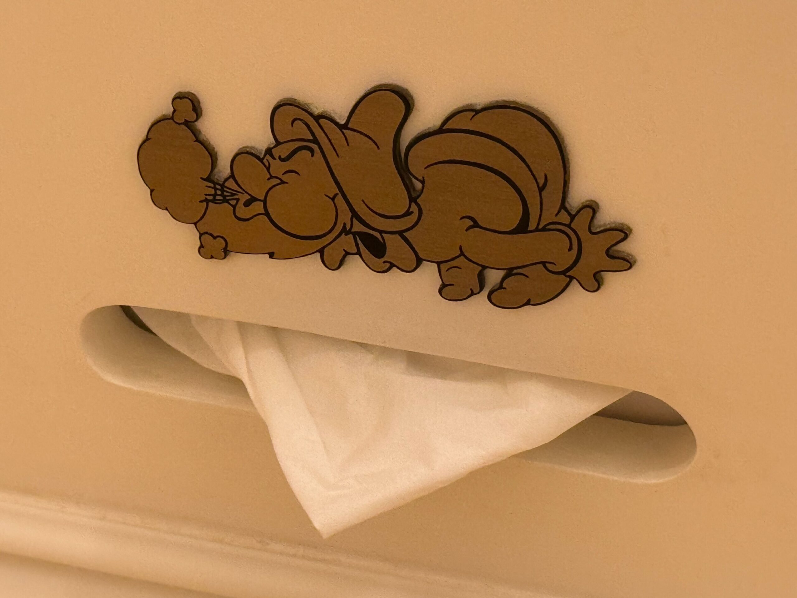 A cartoon character engraved on a piece of furniture in a Deluxe Room at the Hong Kong Disneyland Hotel, with a tissue partially pulled out from a slot below the character.