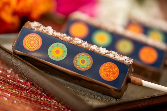 Chocolate-coated dessert bar with decorative floral designs on the surface, placed on a dark rectangular plate, celebrates Hispanic and Latin American Heritage Month.