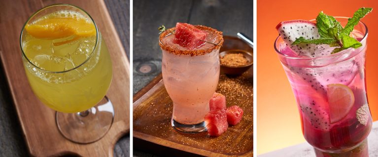 A trio of drinks: a yellow cocktail with an orange slice, a pink drink with a chili-rimmed glass garnished with watermelon, and a purple drink with dragon fruit slices and a mint sprig, perfect for celebrating Hispanic and Latin American Heritage Month.
