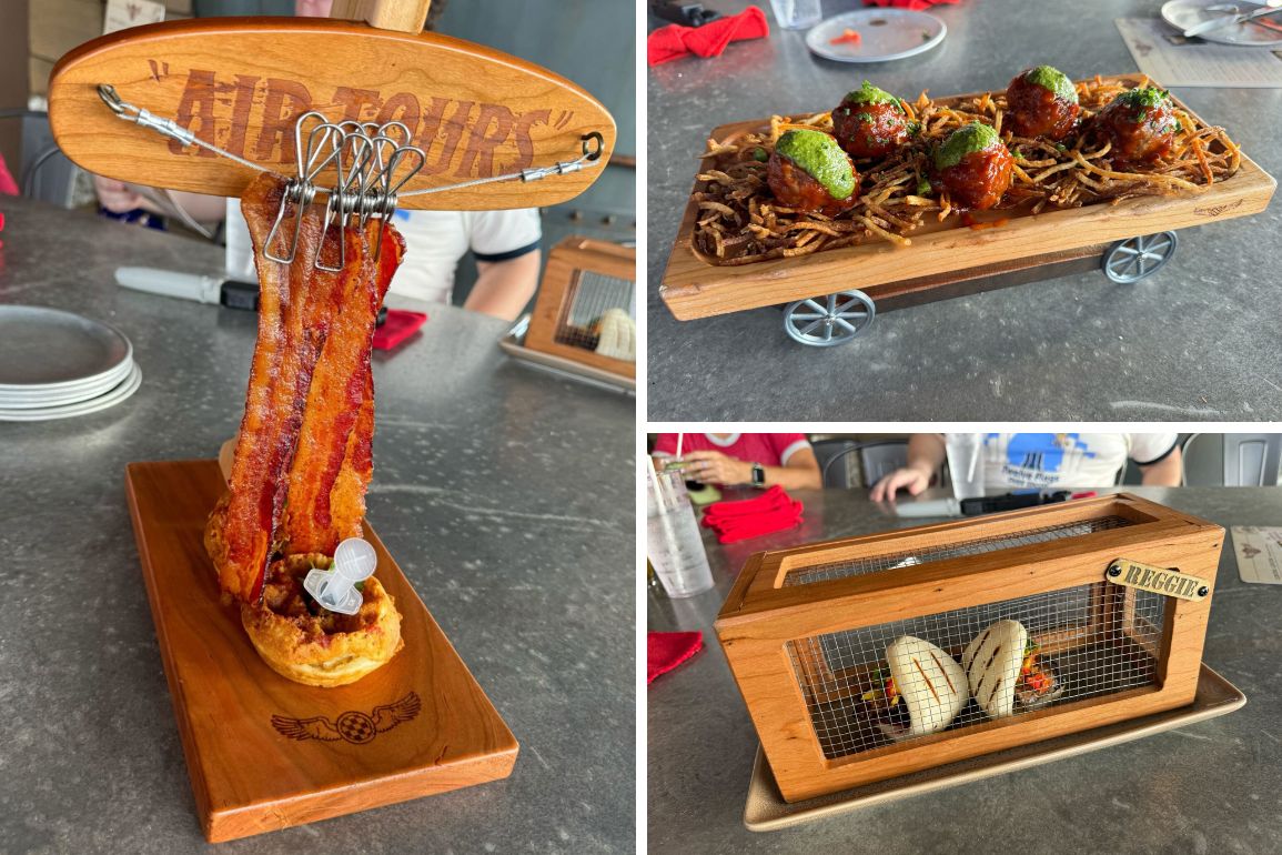 Three gourmet dishes: a bacon presentation on a wood plane, meatballs on a nest-like base, and bao buns in a wooden crate. All placed on a gray surface with people in the background, reminiscent of the adventurous ambiance at Disney Springs' Jock Lindsey's Hangar Bar.