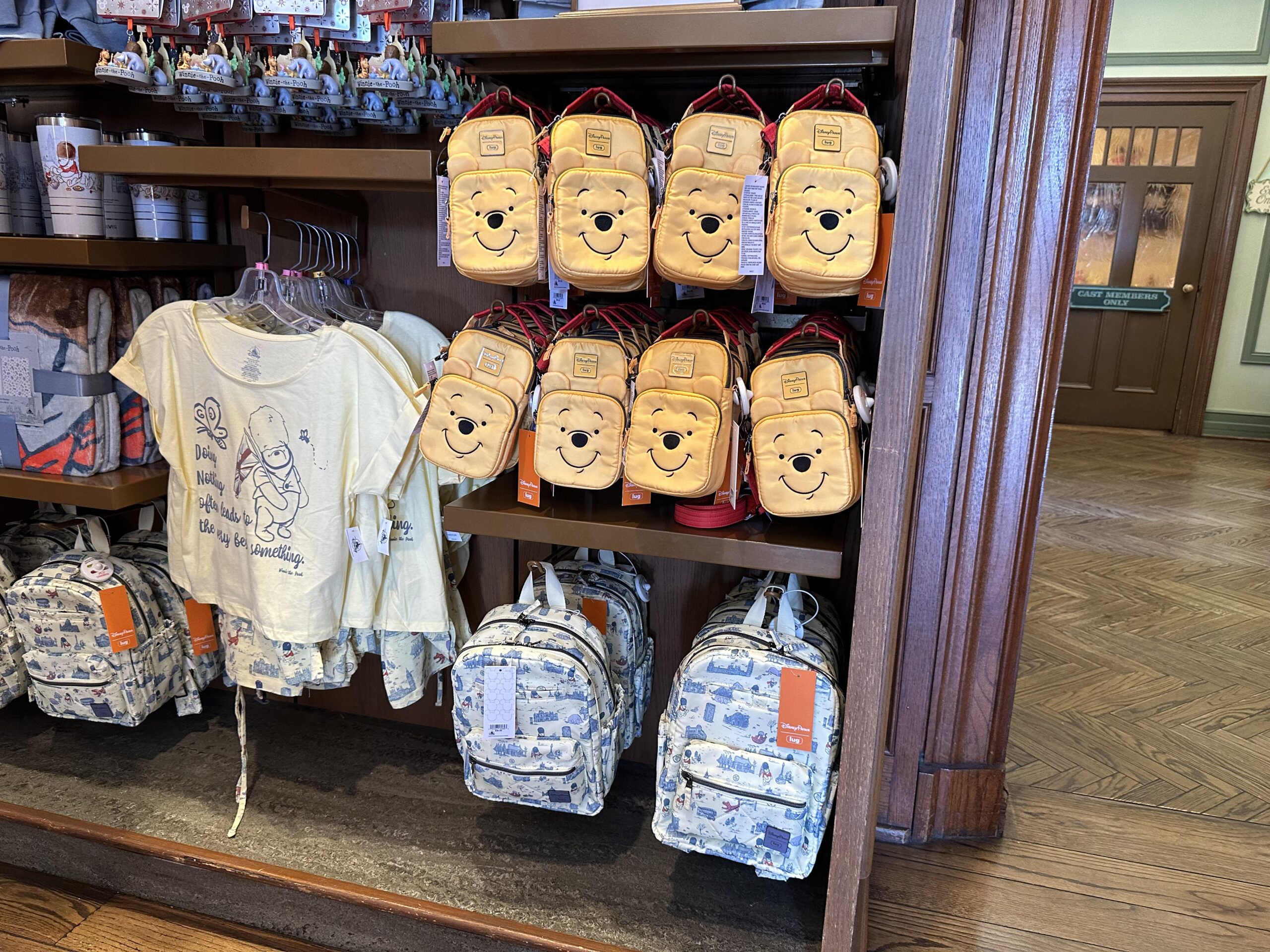 A store display showcasing yellow backpacks with a bear face, white backpacks with a blue pattern, and yellow short-sleeve shirts featuring a cartoon bear and text.