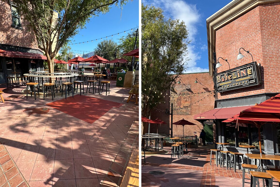 Outdoor patio of a restaurant with empty tables and chairs under string lights and red umbrellas. A sign reading "Baseline" is on the brick wall of the building. Trees provide partial shade.