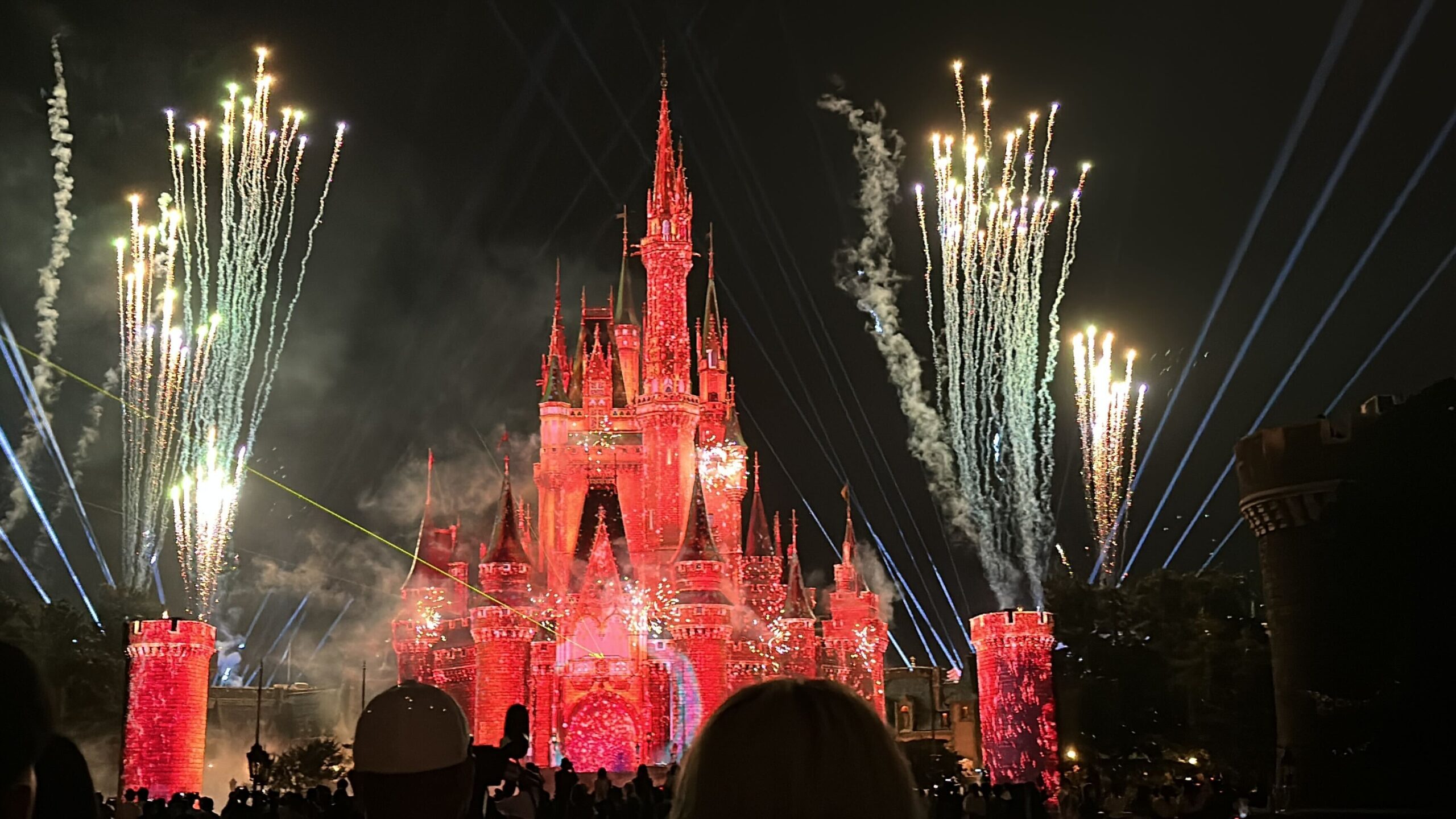 A castle illuminated in red at night with fireworks, light beams, and smoke effects in the background; a crowd is gathered in the foreground, as if ready to reach for the stars.