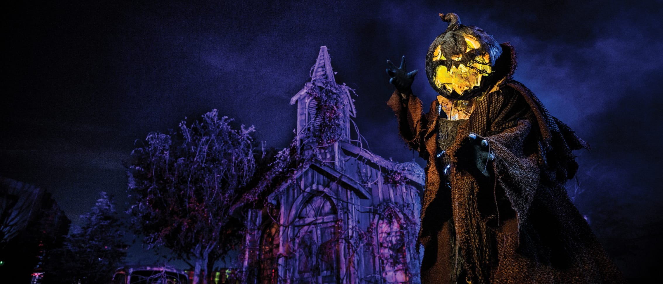 A figure wearing a pumpkin-shaped mask and a tattered robe stands in front of a spooky, dilapidated house with a dark, eerie background, reminiscent of the haunting scenes you might find at Universal Orlando during their Halloween events for Annual Passholders.