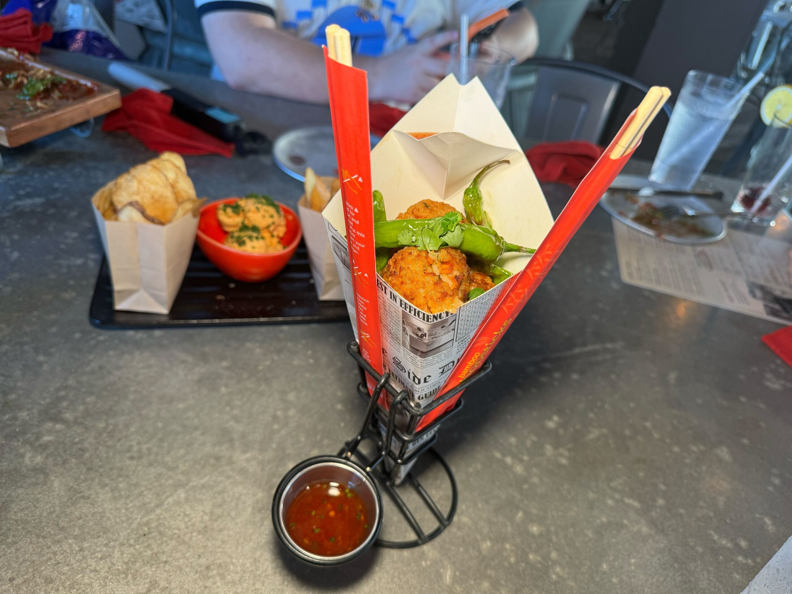 A table at Disney Springs boasts a serving of food, including an appetizer in a red container lined with paper, a small dish of sauce, and another side dish in a red bowl with bread, reminiscent of the offerings at Jock Lindsey's Hangar Bar.