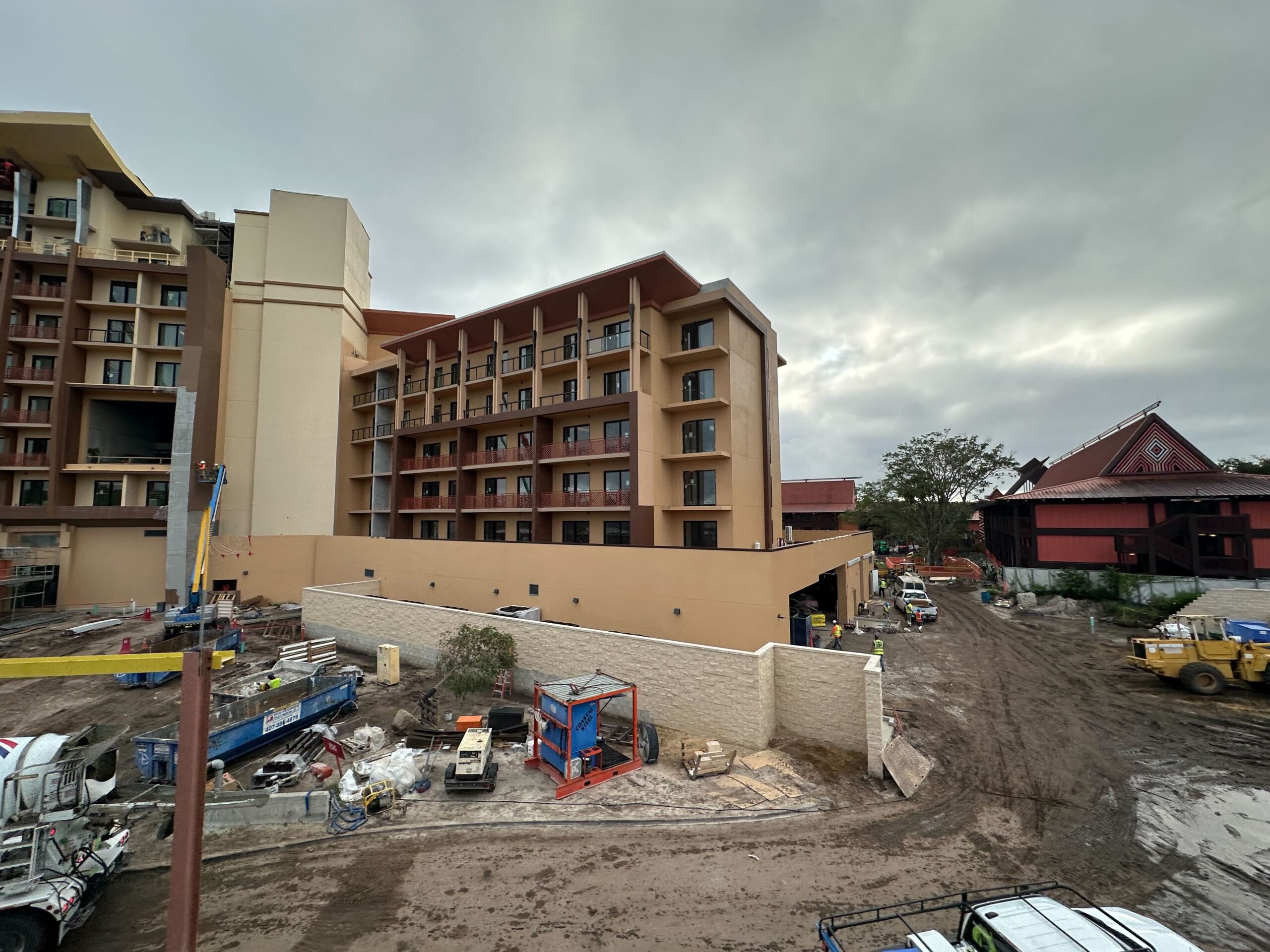 Construction site of a multi-story building with heavy machinery, workers, and equipment visible; cloudy sky overhead.