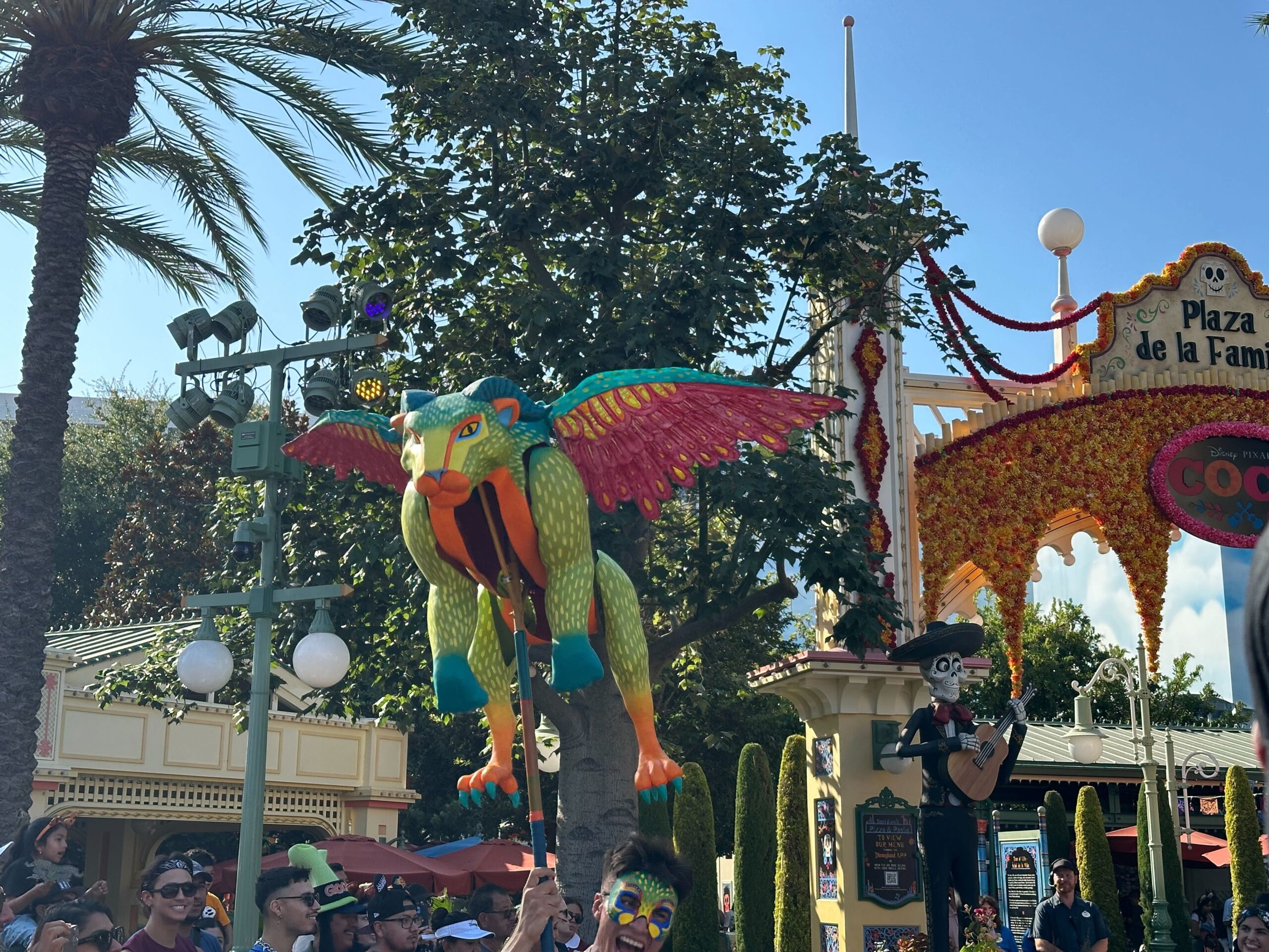 Colorful winged creature puppet held by a performer at a festive outdoor event.
