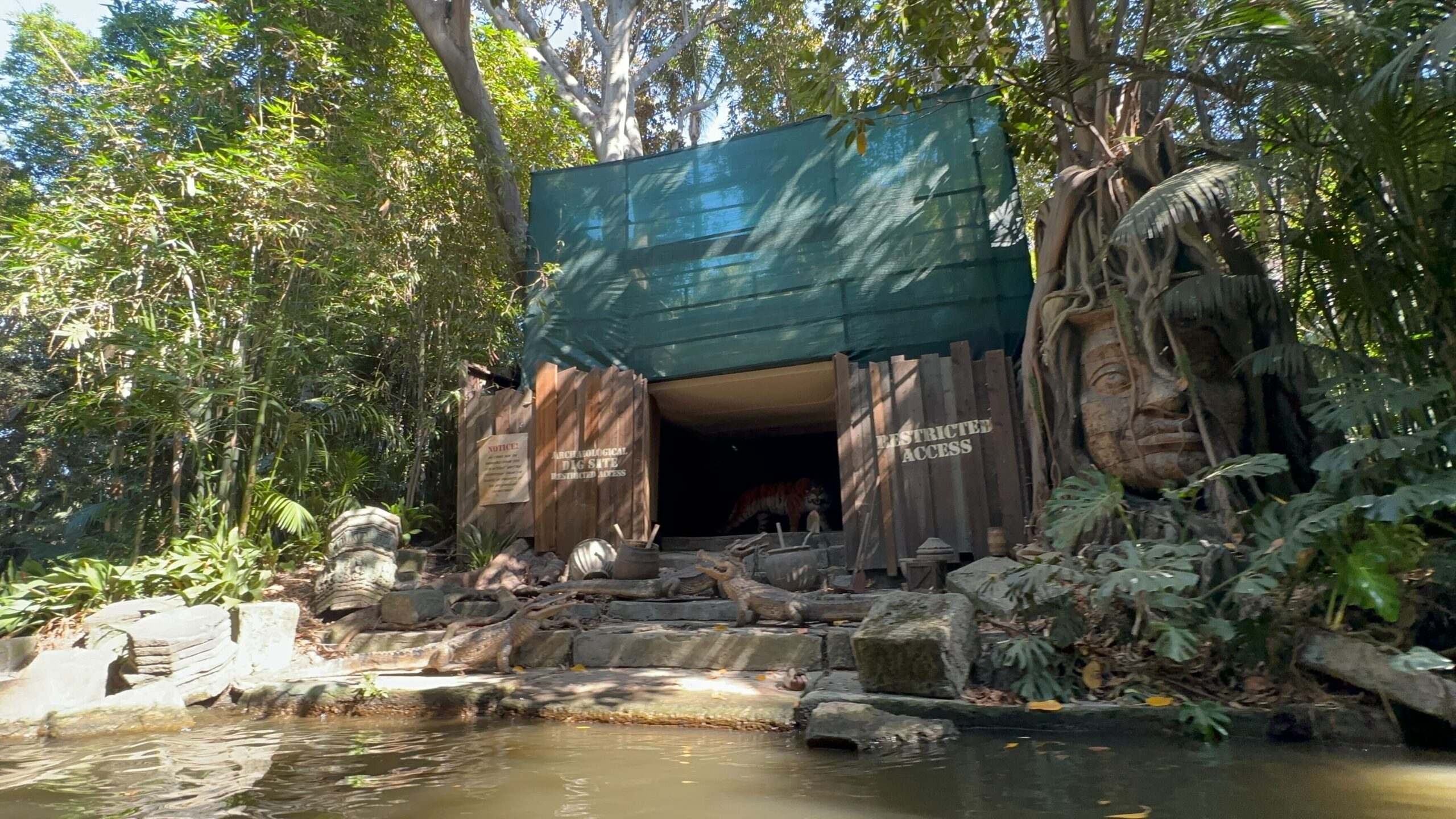 A jungle-themed entrance with wooden doors labeled "Cast Members & Facilities" and "Facilities, Cast Members Only." A large tree and stone statue are visible.
