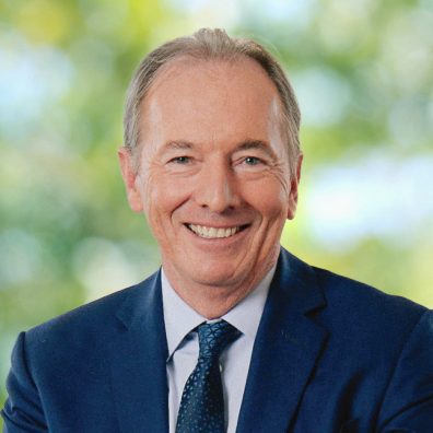 James Gorman, in a suit and tie, is smiling against a blurred green background.