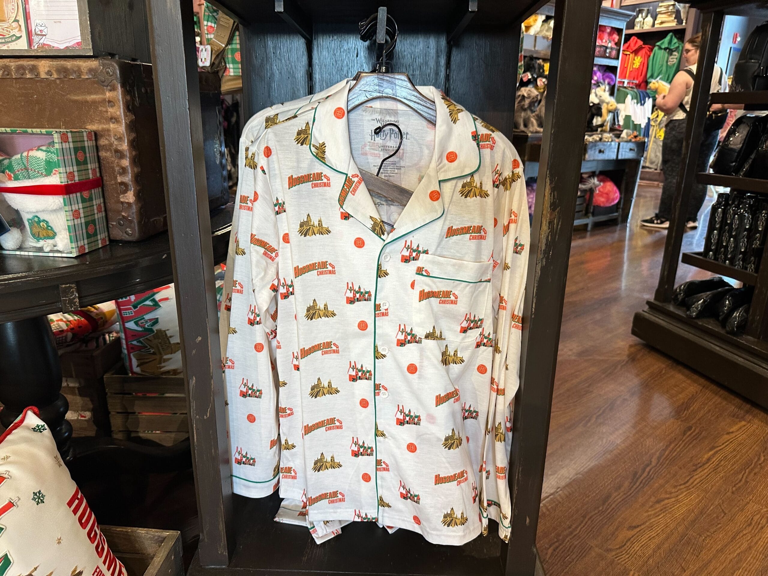 White pajamas with a holiday-themed print, featuring text and small festive graphics reminiscent of winter nights in Hogsmeade, displayed on a wooden rack in a store. White pajamas with a holiday-themed print, featuring text and small festive graphics reminiscent of winter nights in Hogsmeade, displayed on a wooden rack in a store.