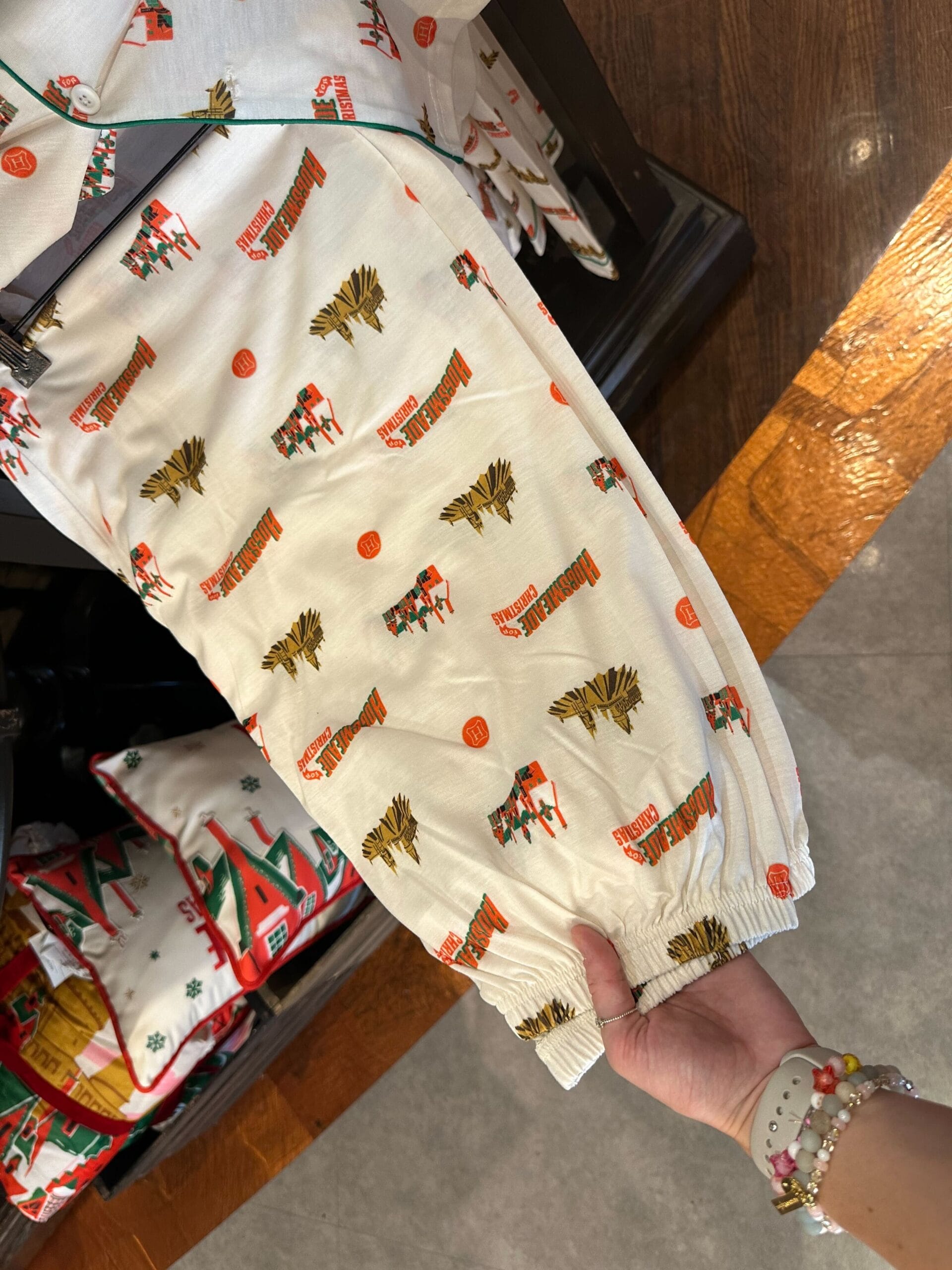 A hand gently holds a white fabric adorned with red "Merry Christmas" text and reindeer print, reminiscent of the cozy charm found in Hogsmeade, as it rests next to a wooden floor. A hand gently holds a white fabric adorned with red "Merry Christmas" text and reindeer print, reminiscent of the cozy charm found in Hogsmeade, as it rests next to a wooden floor.