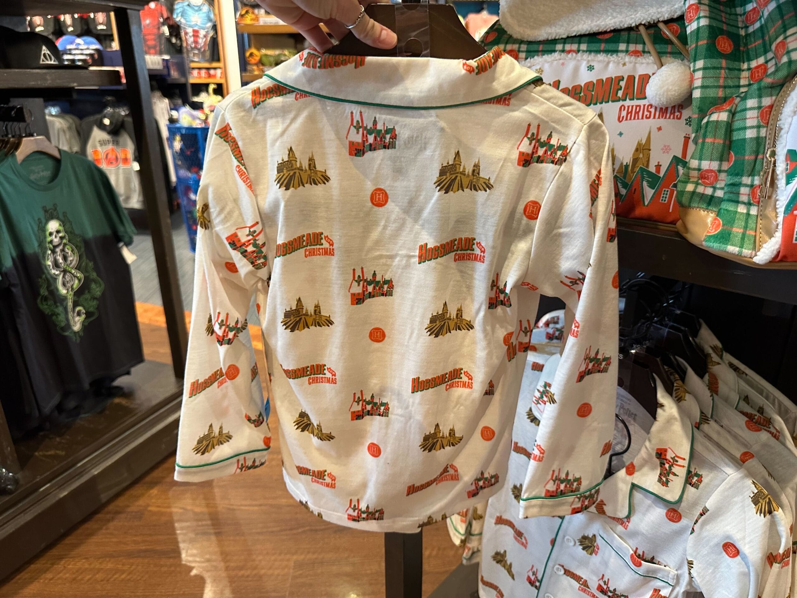Children's pajama top adorned with enchanting holiday-themed illustrations, featuring the "Hogsmeade Christmas" text, displayed on a store rack. Children's pajama top adorned with enchanting holiday-themed illustrations, featuring the "Hogsmeade Christmas" text, displayed on a store rack.