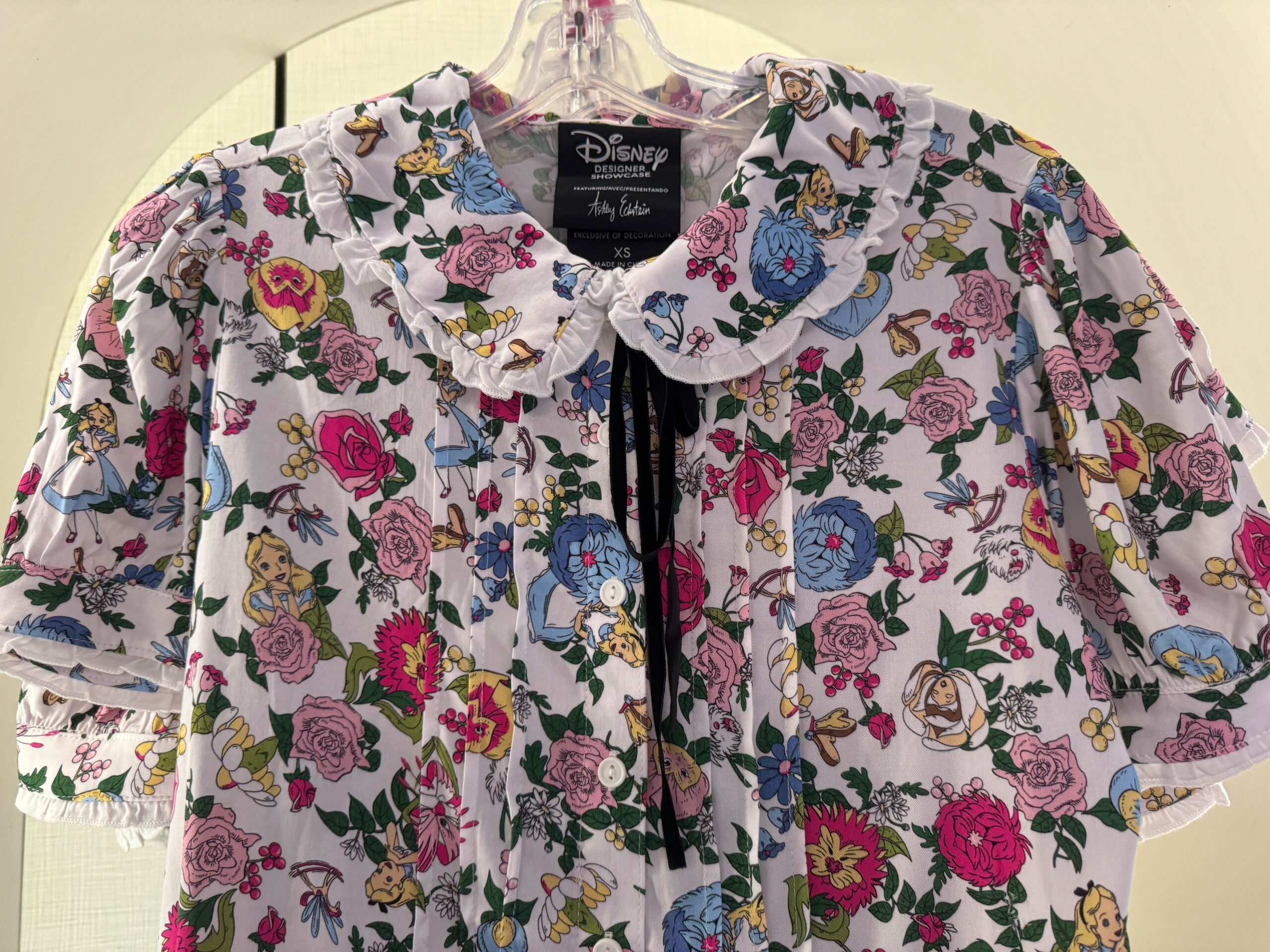 Disney-themed dress with a floral and character print featuring pastel colors, hanging on a clear hanger.