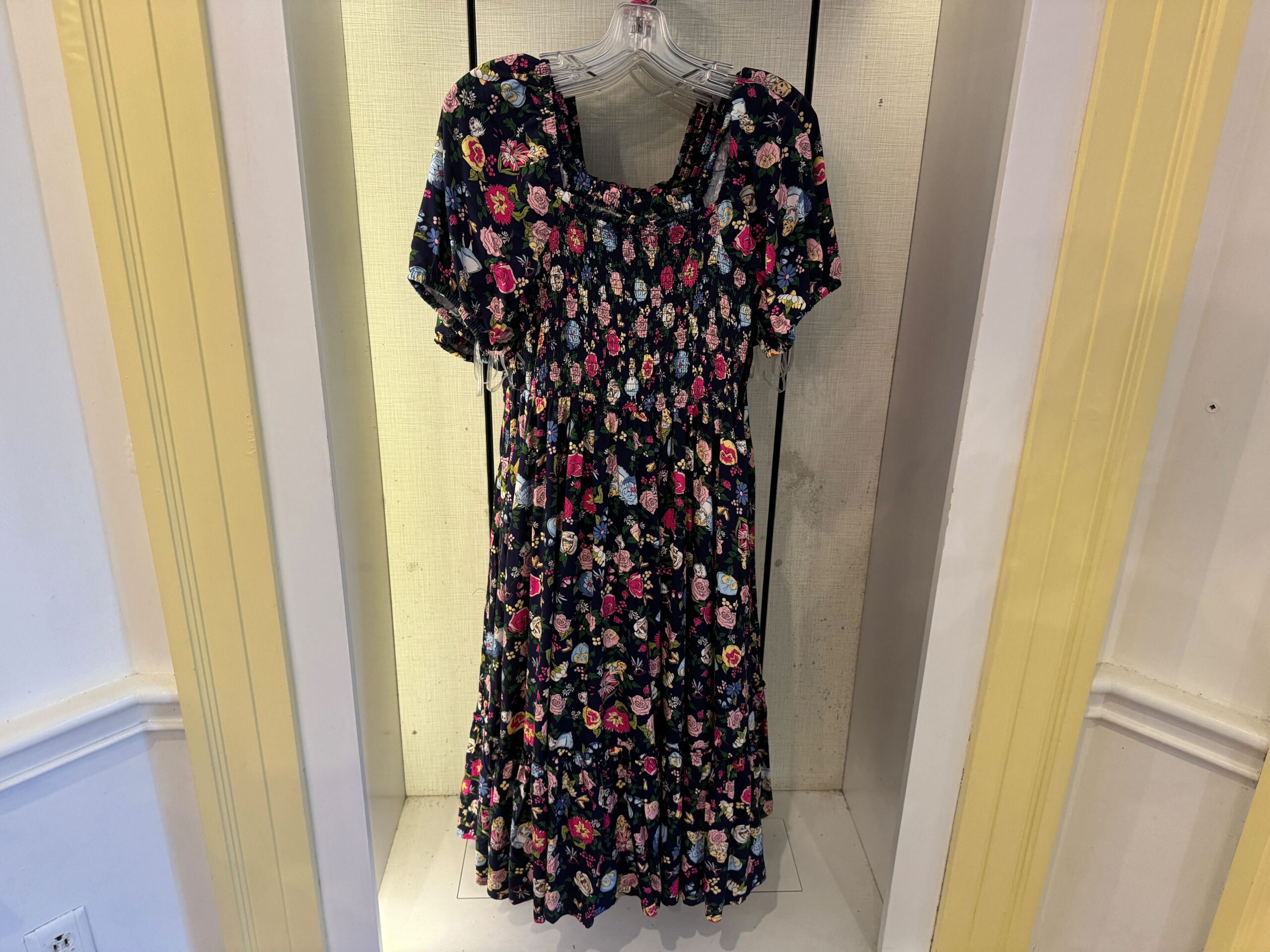 A floral print dress displayed on a hanger in a lighted showcase. The dress has short sleeves and a fitted bodice with a full skirt.
