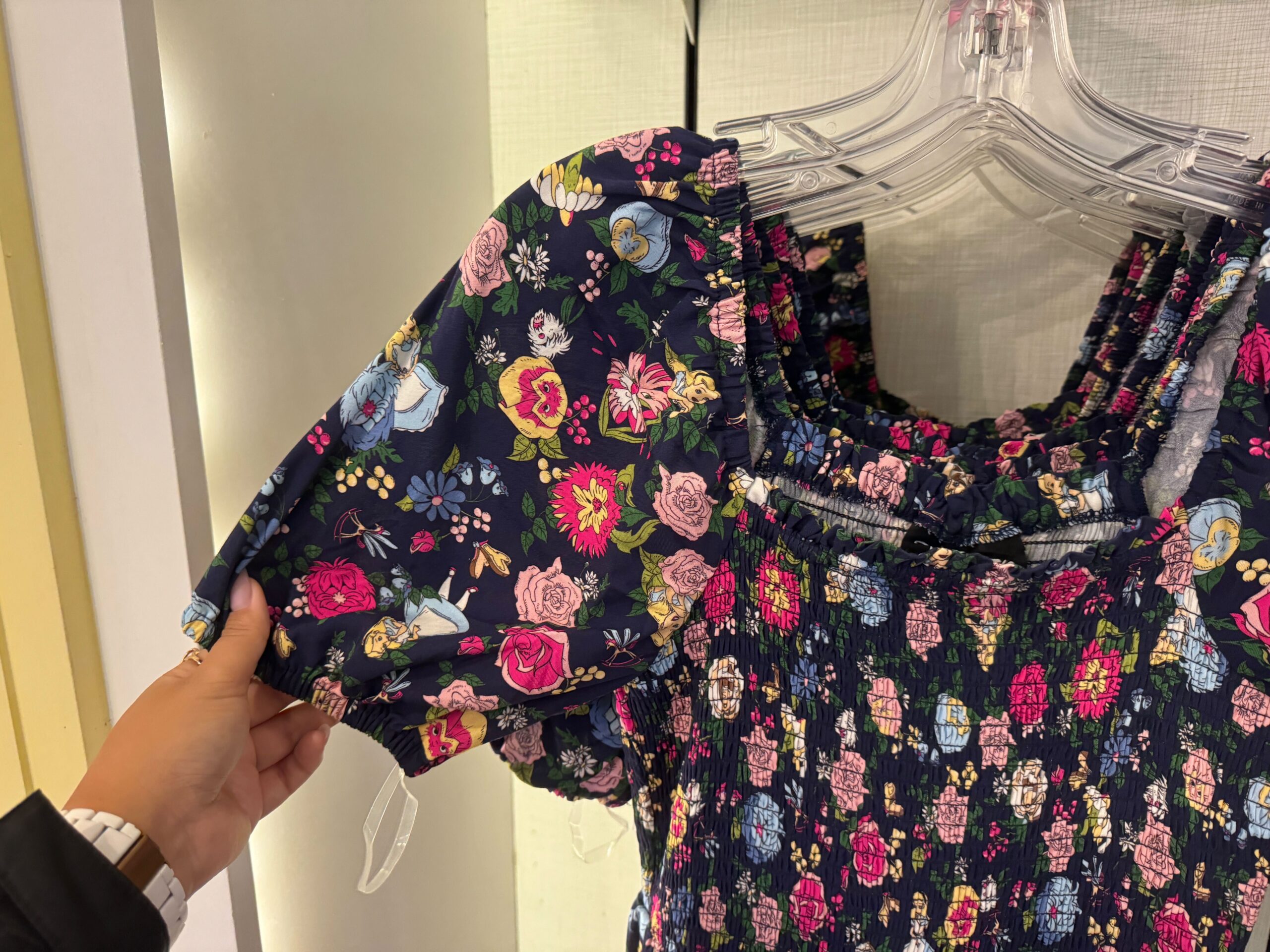 A person holds a dress with a colorful floral pattern, hung on clear plastic hangers.