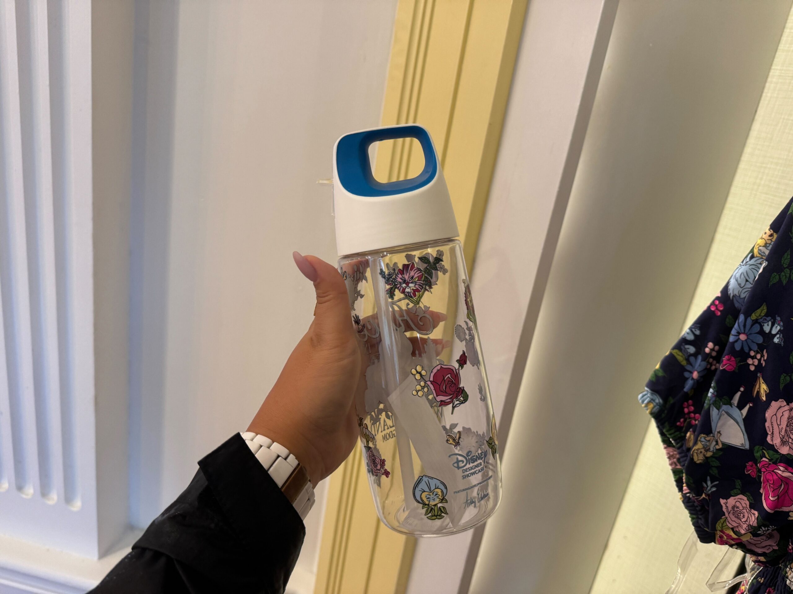 A person holds a transparent water bottle with a blue and white lid, decorated with floral patterns.