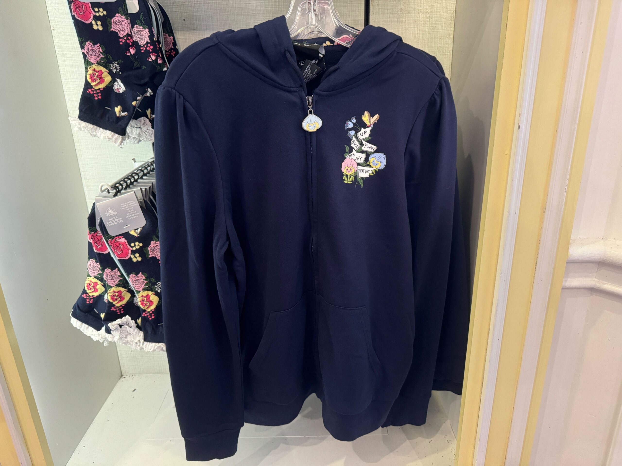A navy blue hooded sweatshirt with a floral embroidery design hanging on a rack alongside floral-patterned clothing.
