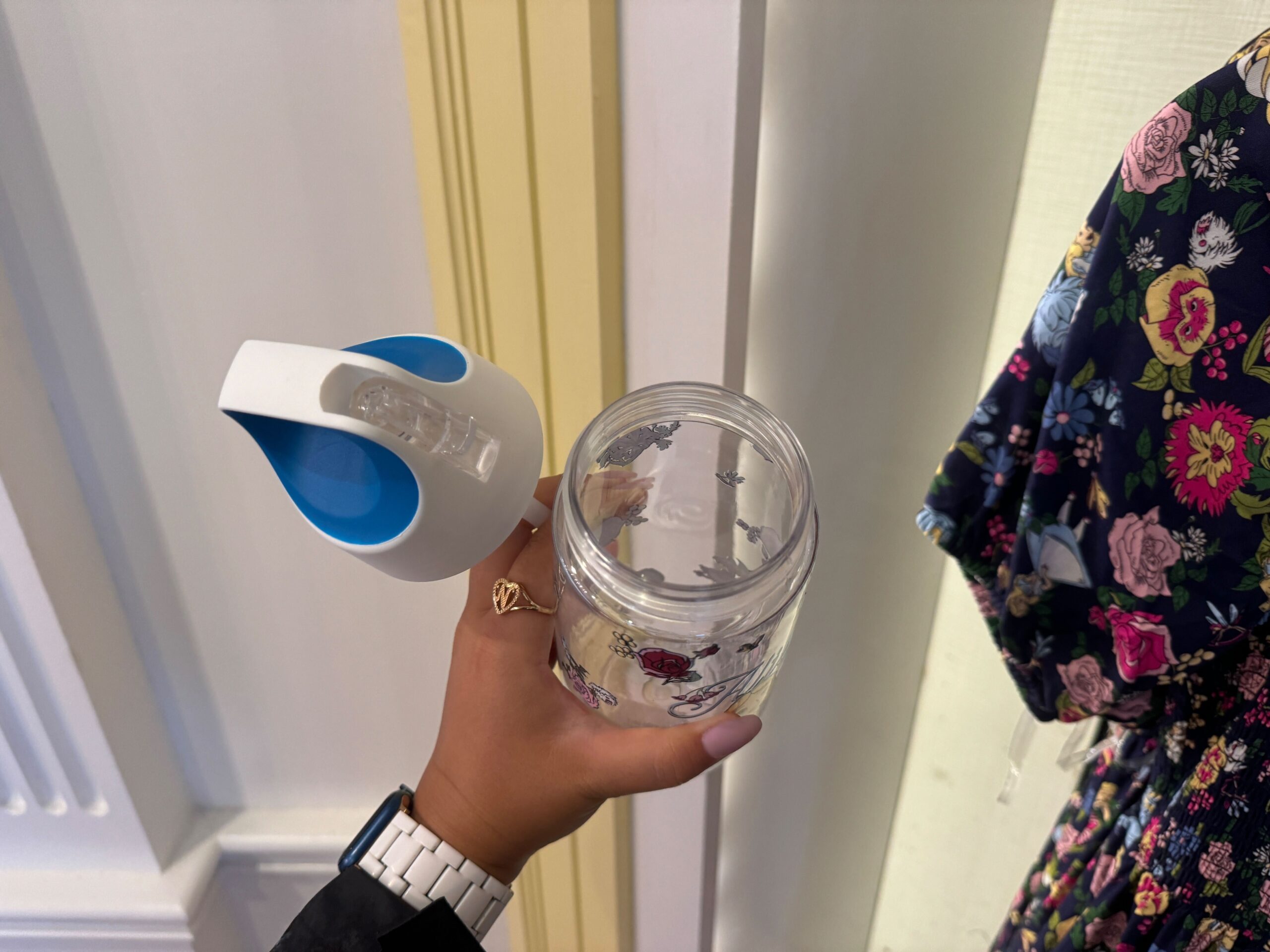 A person holds a transparent plastic bottle with a colorful floral design and a detachable white and blue lid.