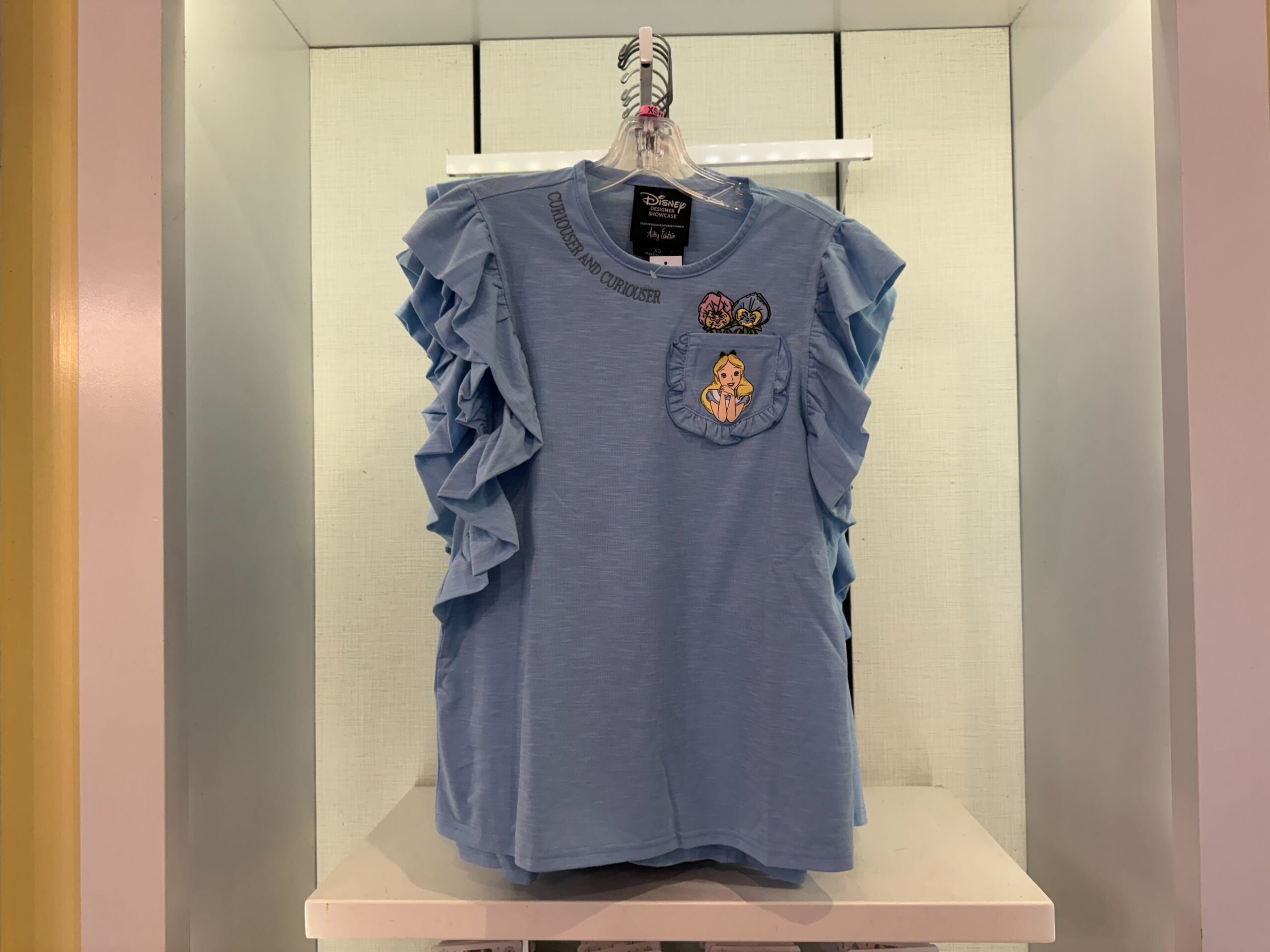 Light blue ruffle-sleeve shirt with a "Courage & Kindness" text, embroidered princess on the pocket, and Disney branding displayed on a hanger.