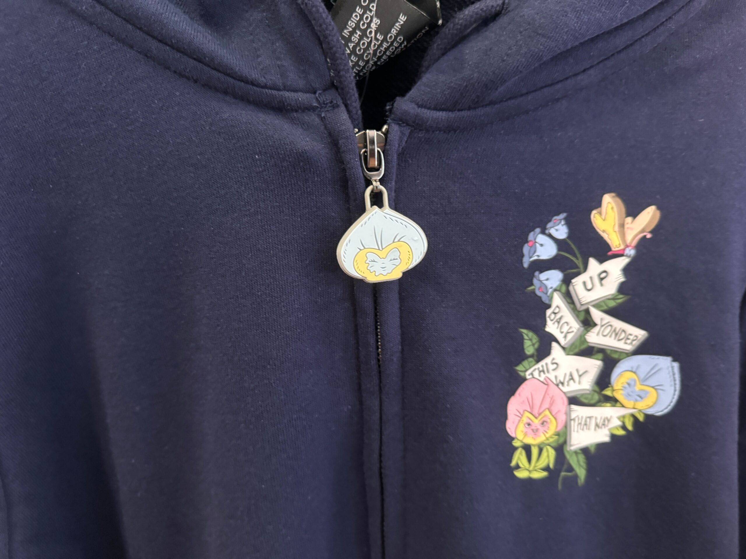 Close-up of a navy hoodie with a flower-themed pendant zipper. The left side features an embroidered design with flowers and the words "Up Back Yonder This Way That Way.