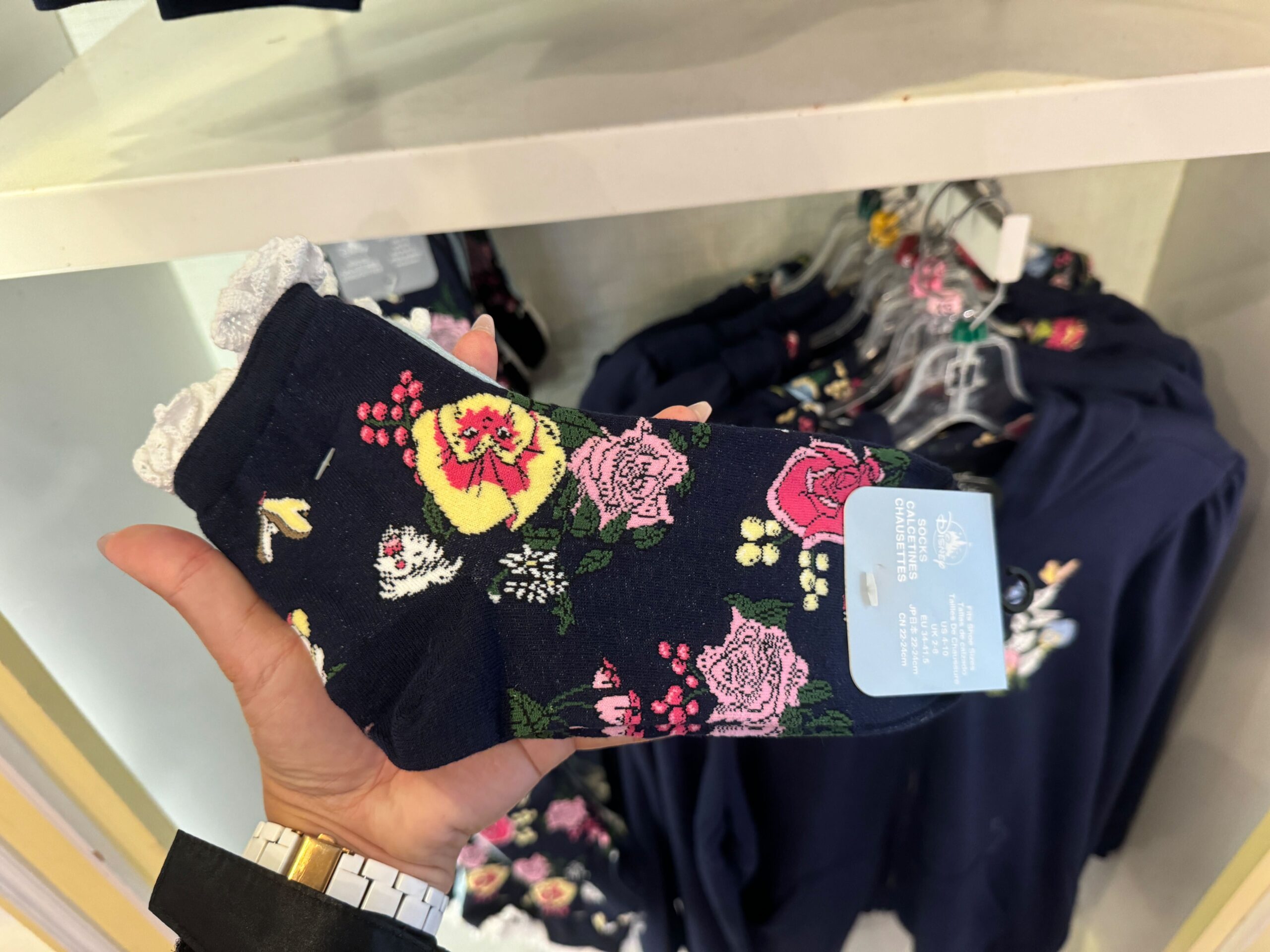 Hand holding a pair of navy blue socks with a floral pattern, displayed in a store setting.