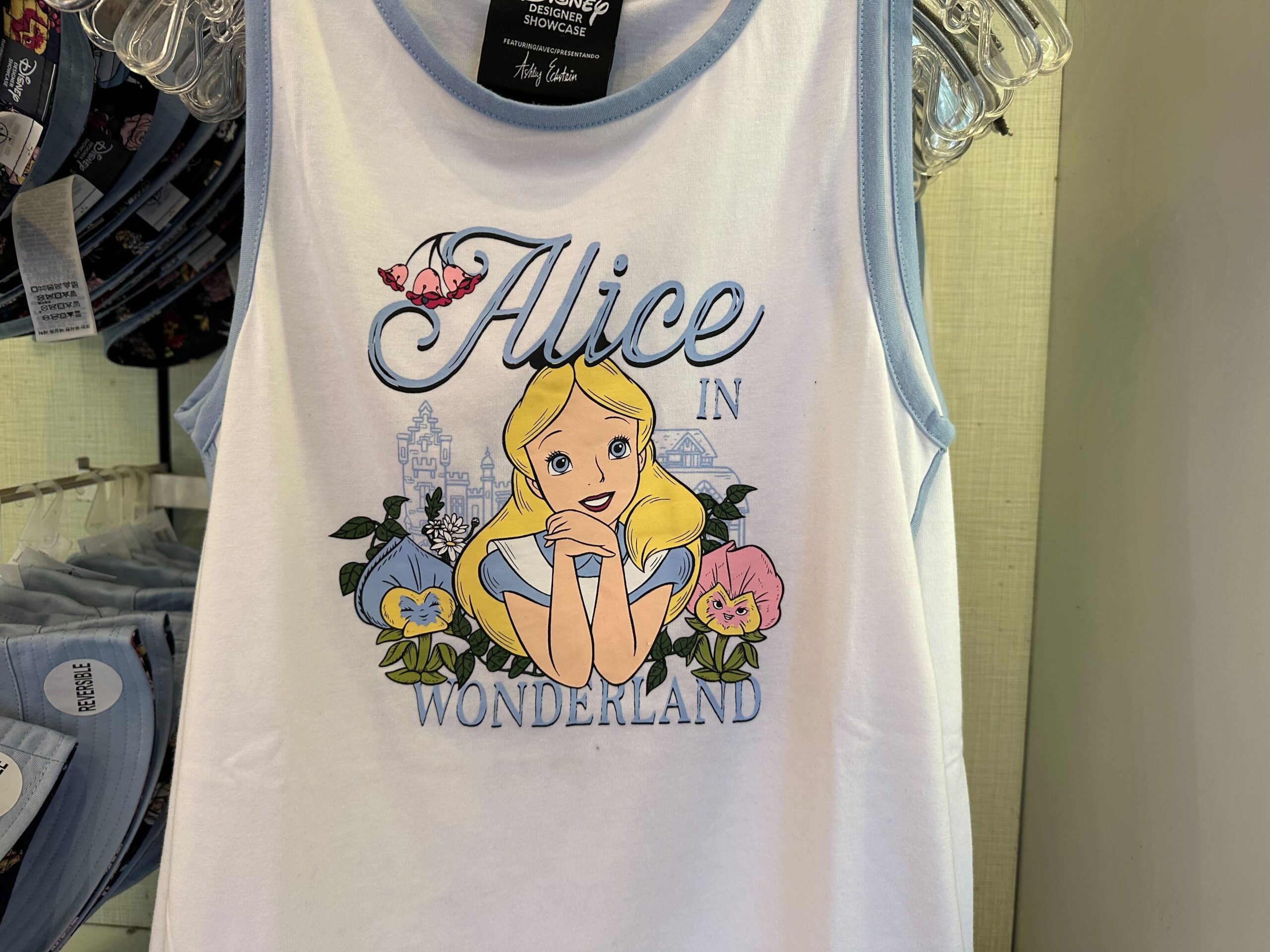 A white tank top with blue trim featuring an illustration of Alice from "Alice in Wonderland," surrounded by flowers—a perfect addition to your Disney Merchandise collection.