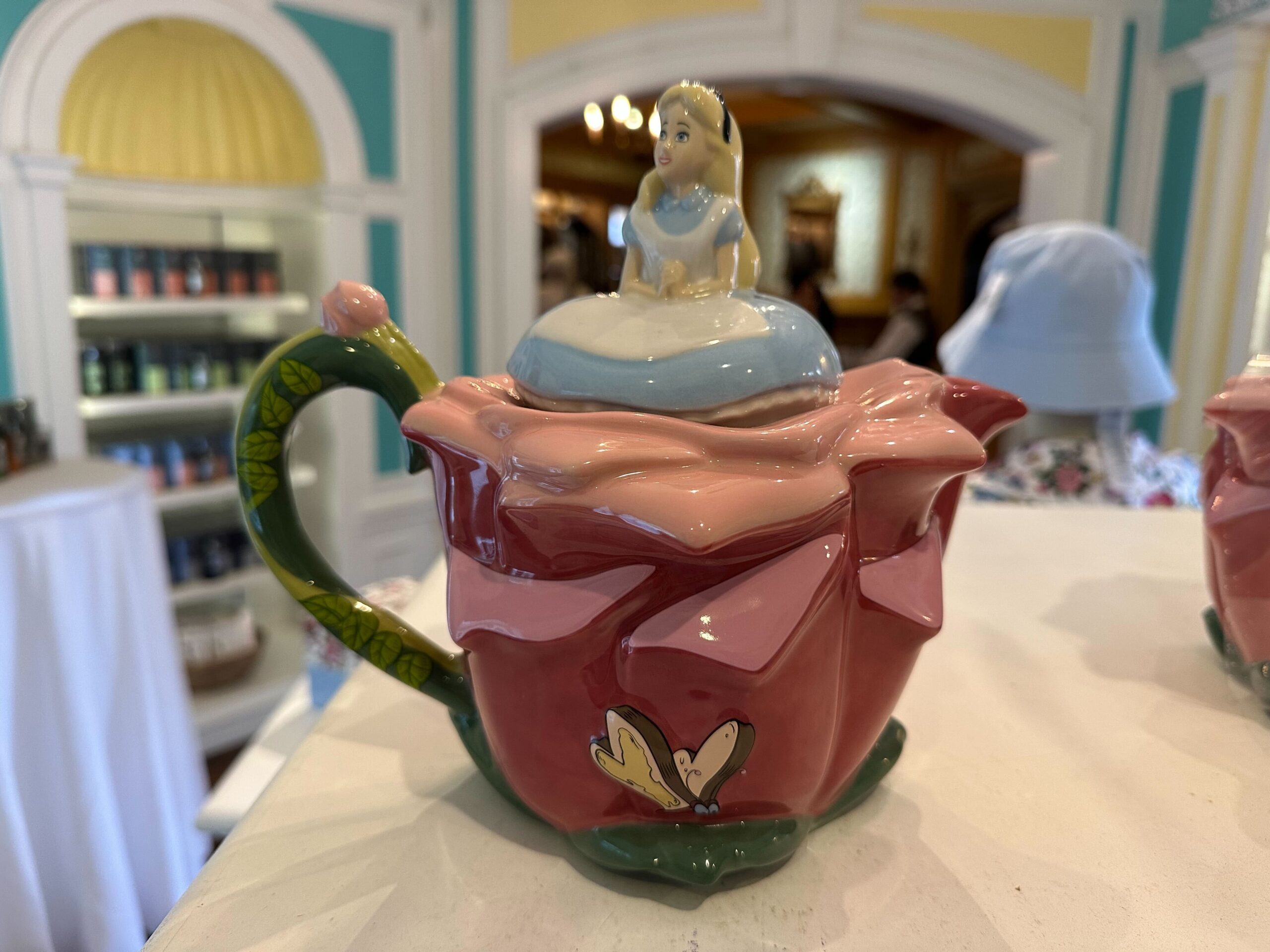 This charming teapot features a whimsical cartoon character reminiscent of "Alice in Wonderland" on top, making it a delightful piece of merchandise for fans and collectors alike.