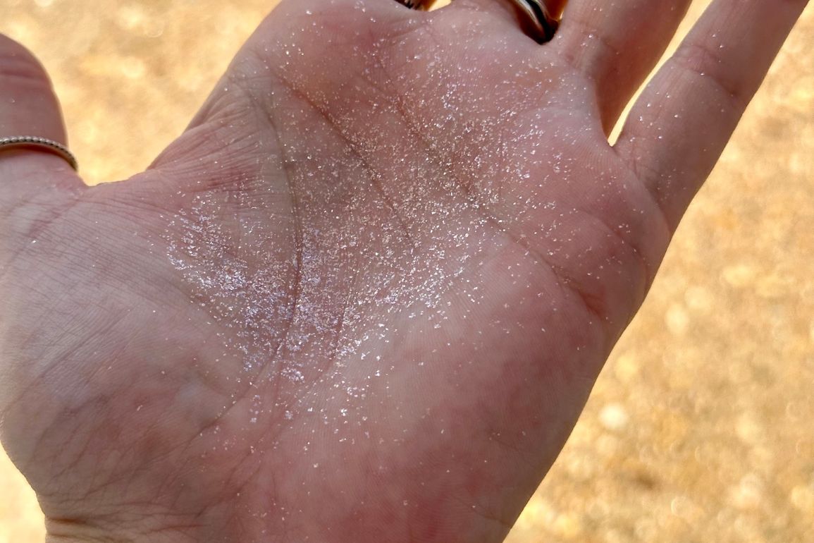 A close-up of an open hand with a layer of fine, sparkly sand covering the palm.