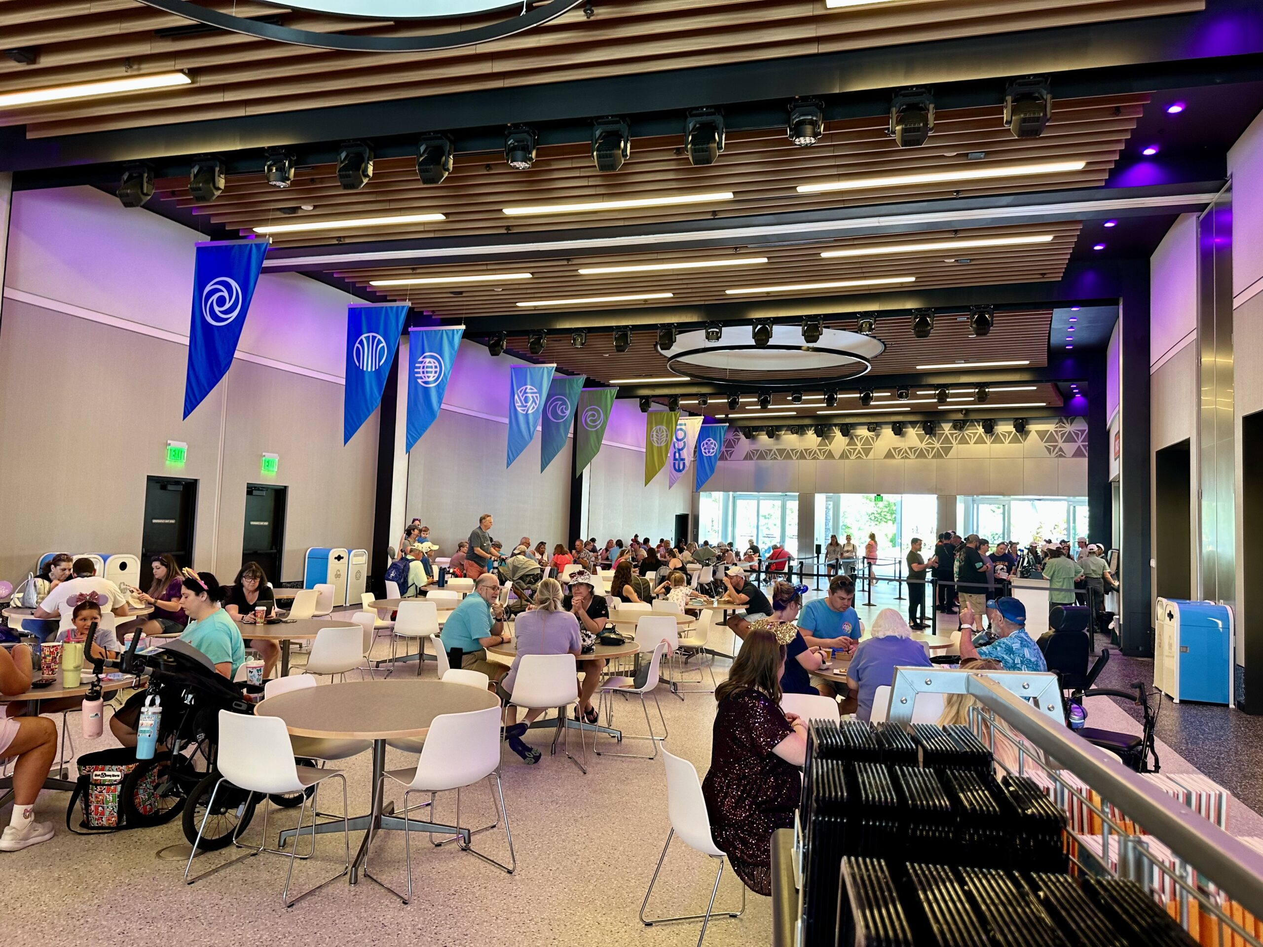 People dining and socializing in a large, modern cafeteria with colorful banners and circular tables.
