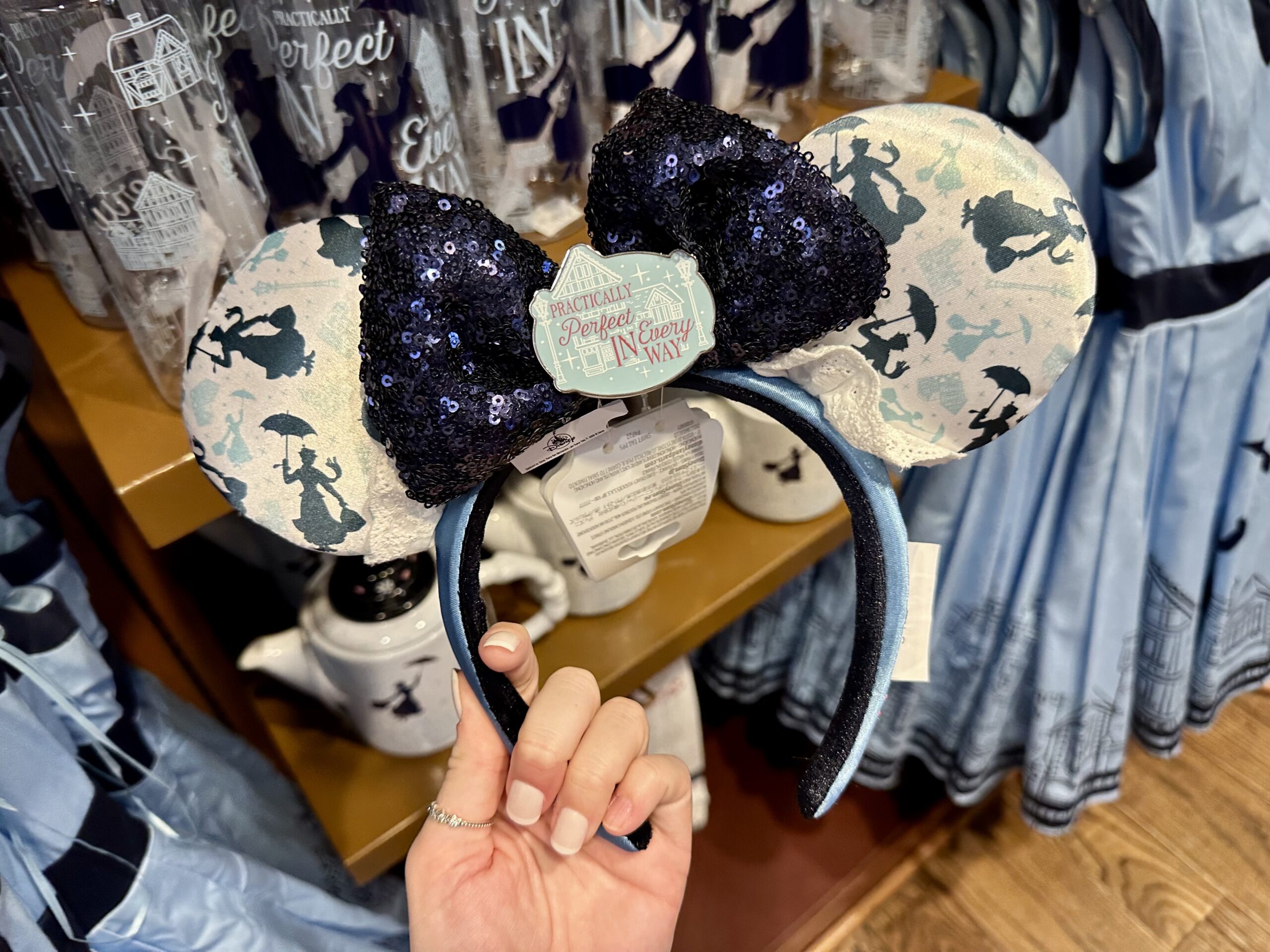 A hand holds a pair of themed Minnie Mouse ears with a sequined bow and printed designs.
