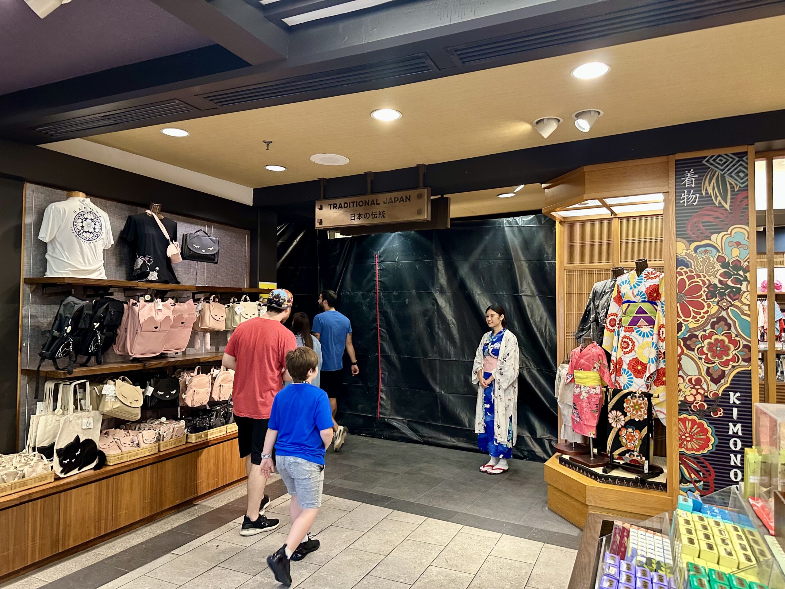 Store interior with bags and clothing on display; people walking by. Woman in a kimono stands near a section under renovation labeled "Traditional Japan.