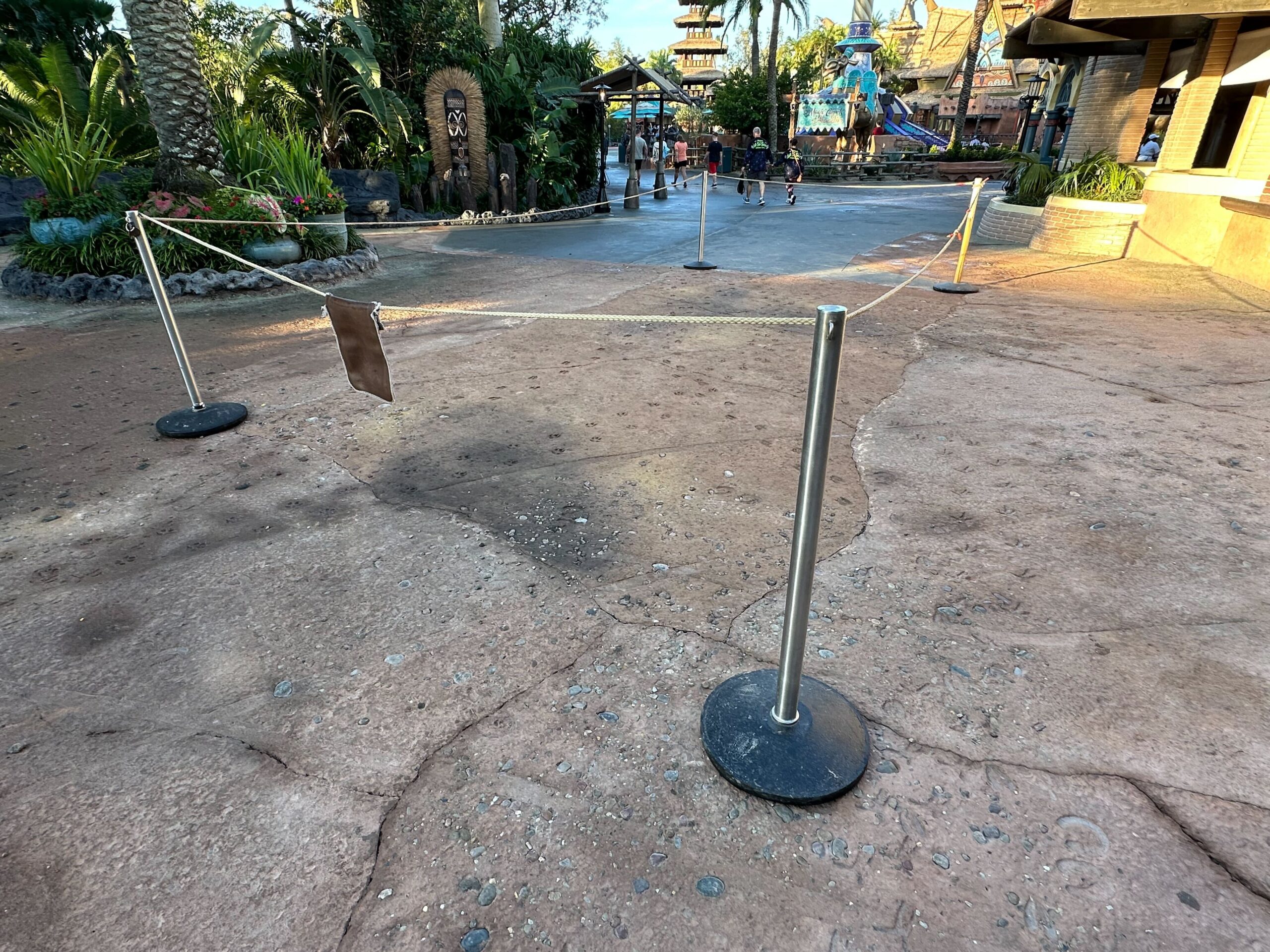 Roped-off area on a theme park pathway with some people walking in the background.