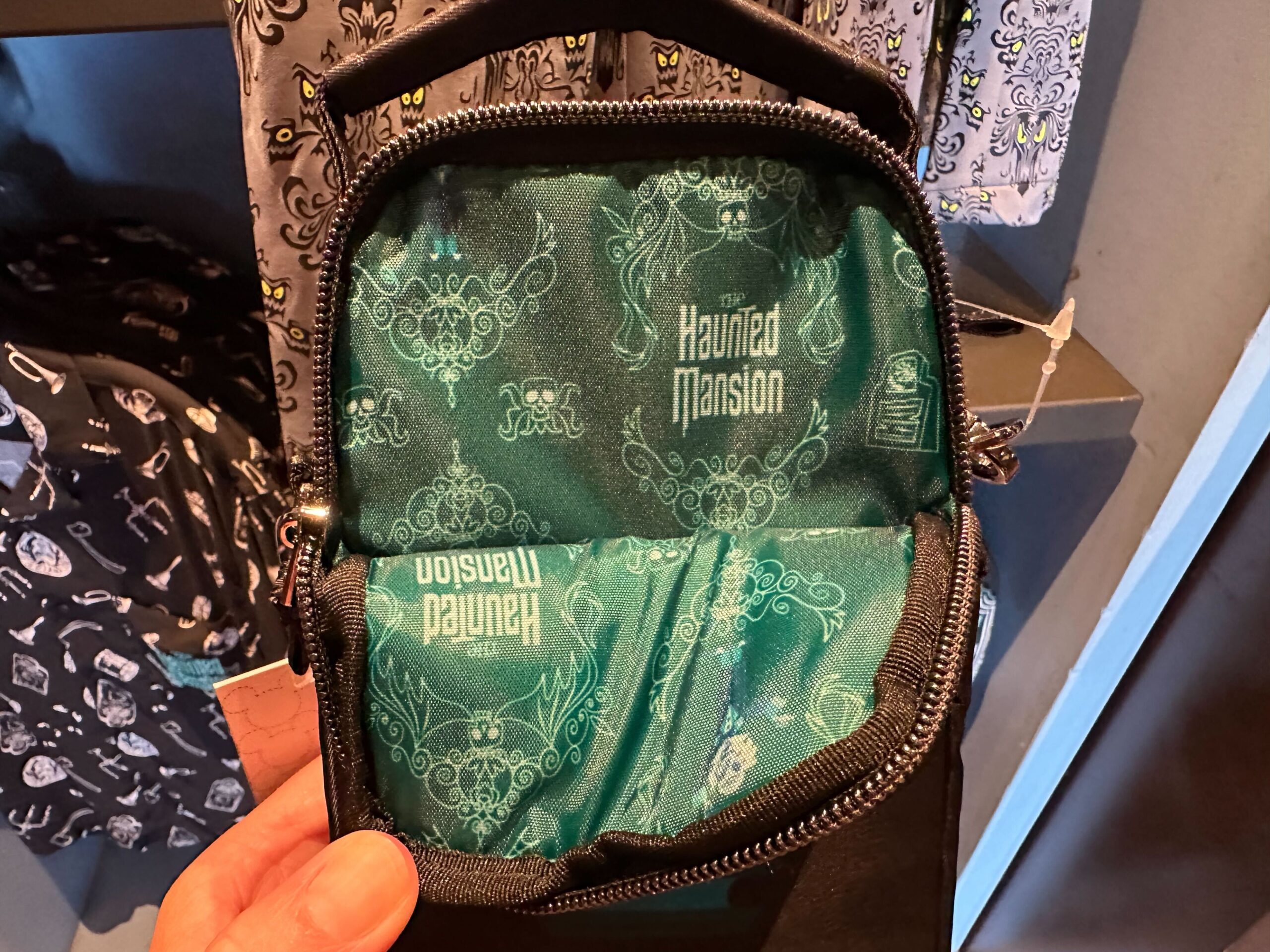 A small, open black bag revealing its teal interior lining, featuring a pattern of white designs and the words "Haunted Mansion.