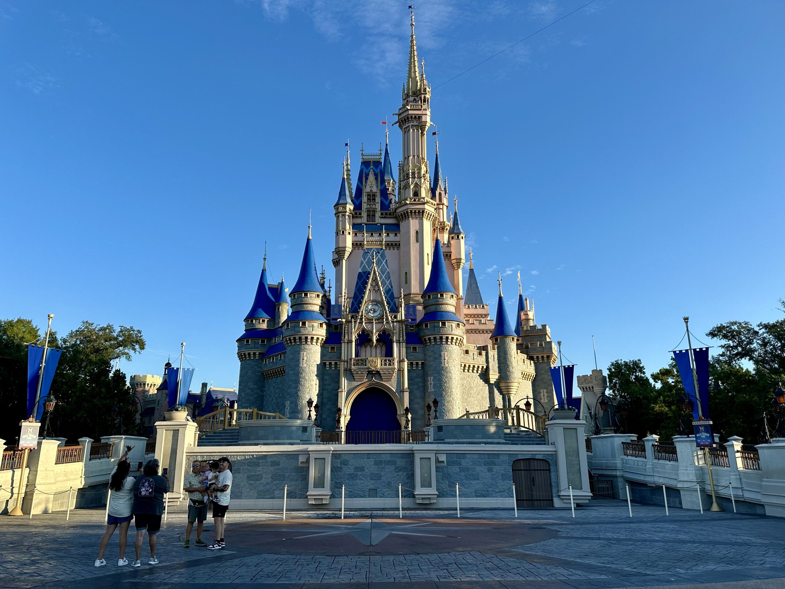 Cinderella Castle at a theme park with blue skies and a few visitors in the foreground.