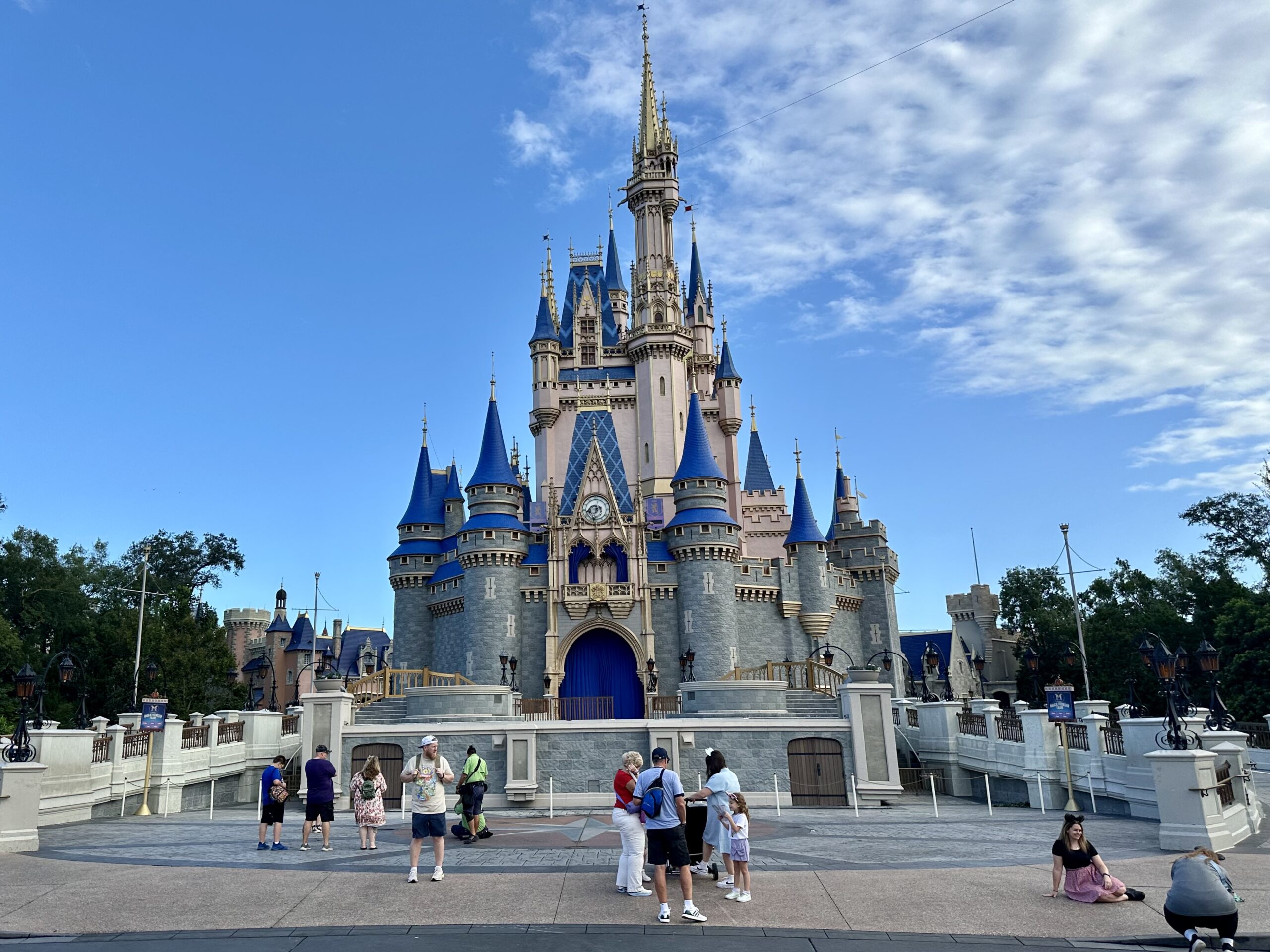 A group of people stand in front of a large castle with blue and gold accents on a sunny day.