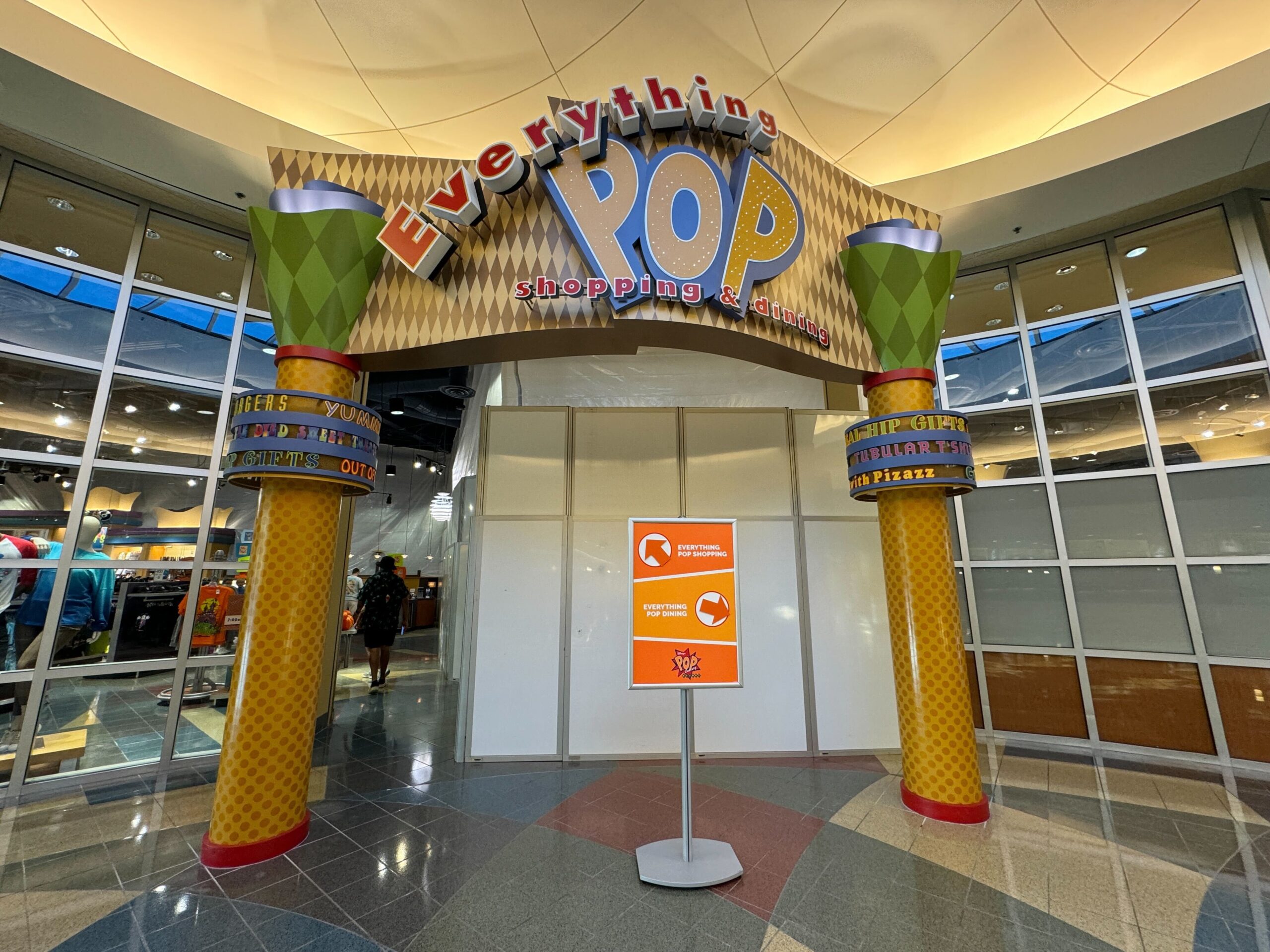 Entrance to "Everything Pop" shopping and dining area with a colorful sign and a smaller sign on a stand, offering directions.