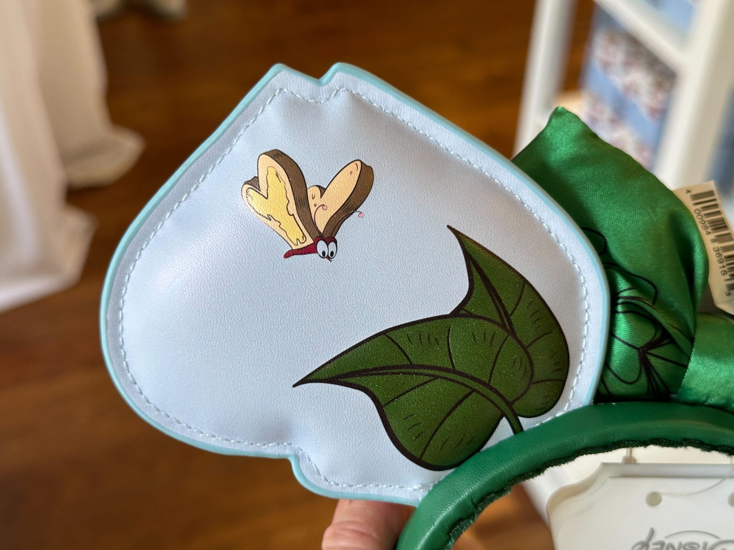 Close-up of a decorative item featuring a playful cartoon butterfly and green leaves on a white background, reminiscent of the whimsical charm found in Alice in Wonderland.