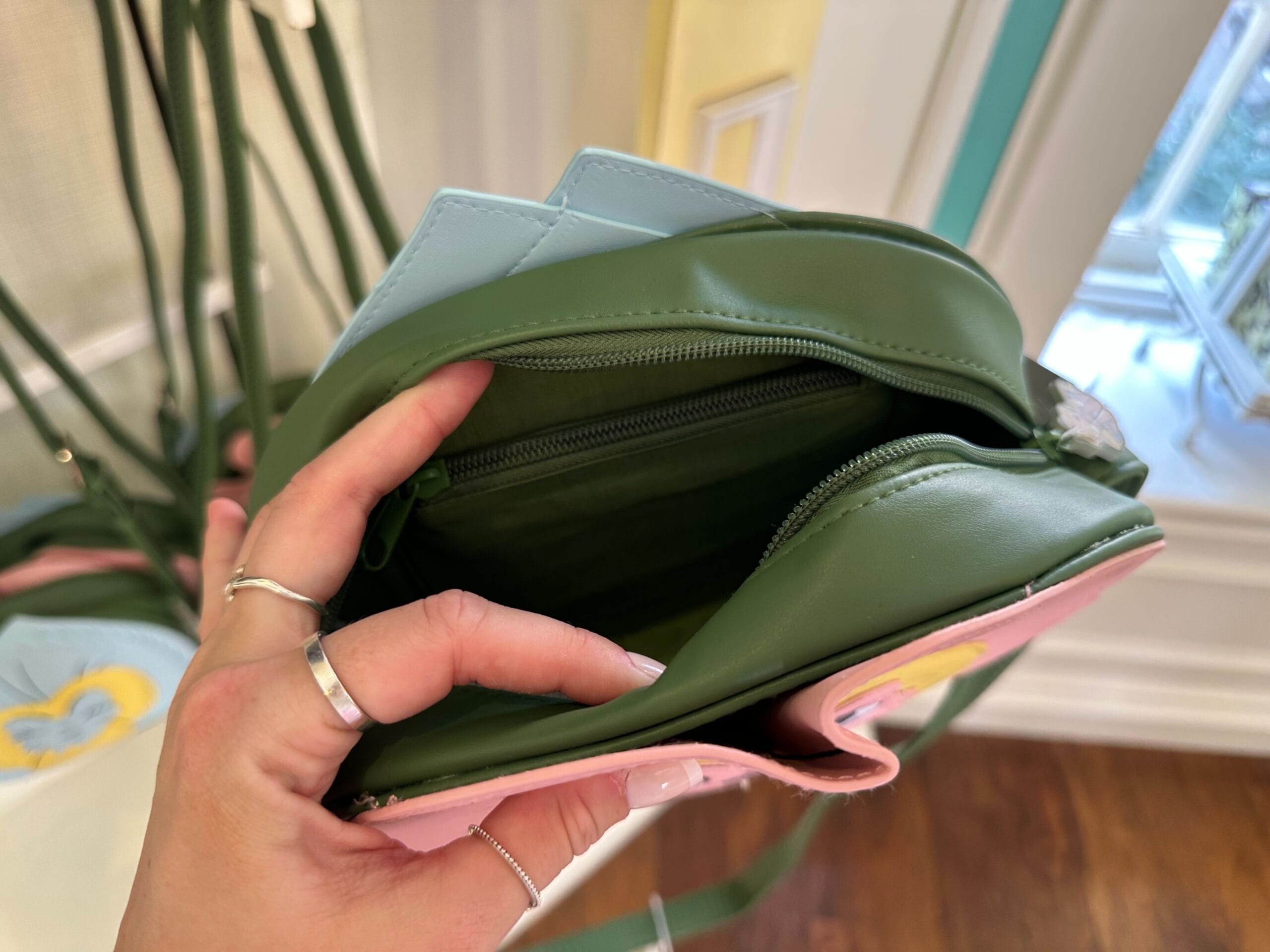 A hand holding an open green wallet with a zipper compartment, intriguingly nestled inside a pink purse, evokes a whimsical touch reminiscent of Alice in Wonderland.