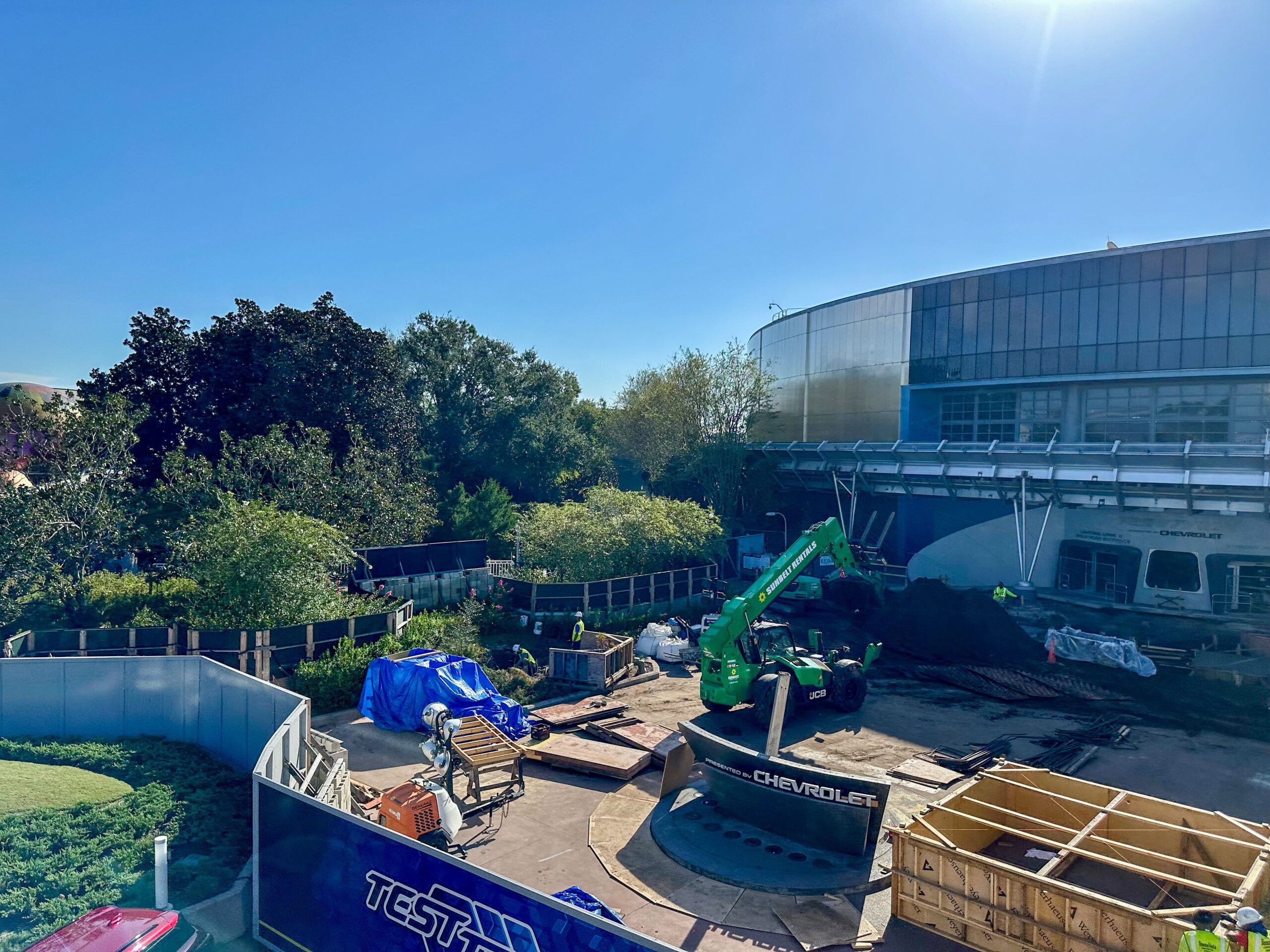 Construction site with a green excavator and materials near a modern building under a clear blue sky.