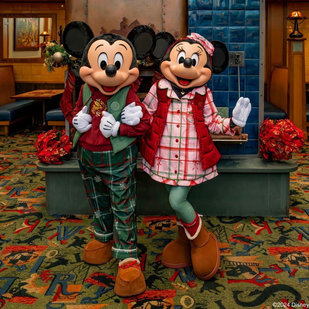 Two characters wearing festive attire: one in green plaid pants and a red vest, the other in a plaid dress with a red vest, standing on a carpeted floor in front of holiday decor.
