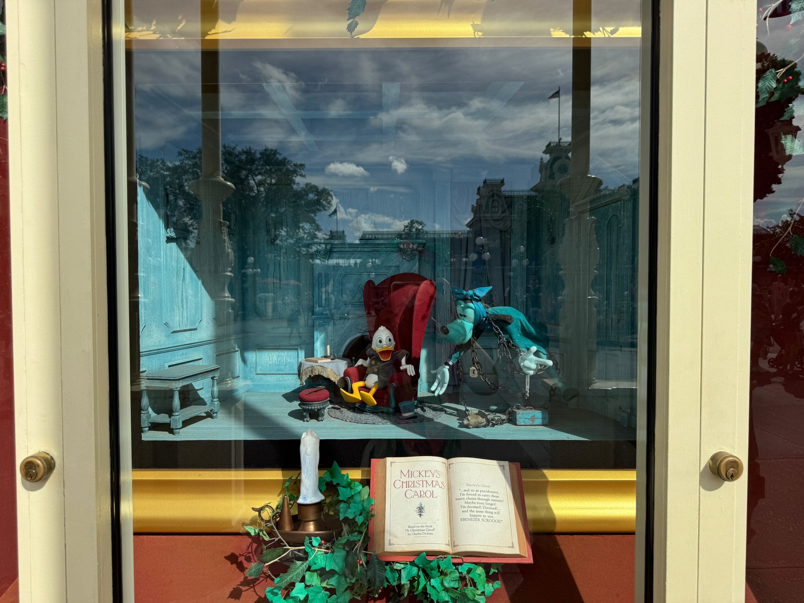 A shop window at the Main Street Emporium showcases a figure in an armchair, with a candle and an open book labeled "Mickey's Christmas Carol.