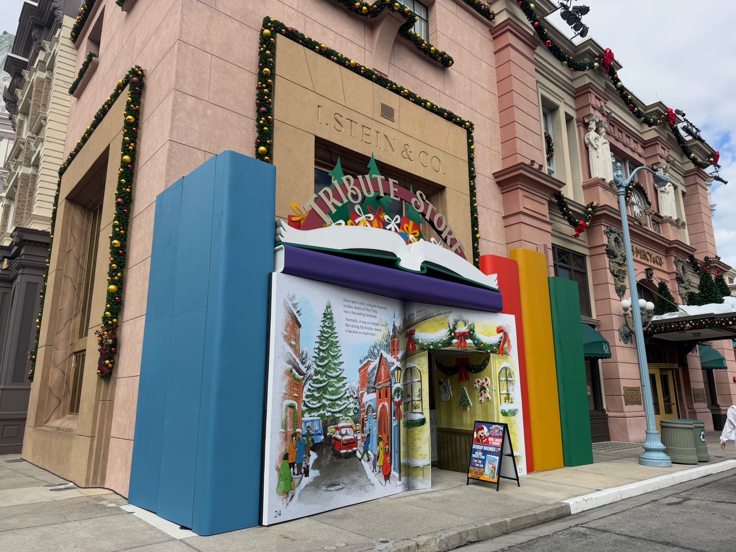 A storefront decorated with colorful books and Christmas ornaments, featuring an entrance shaped like an open storybook in an urban setting.