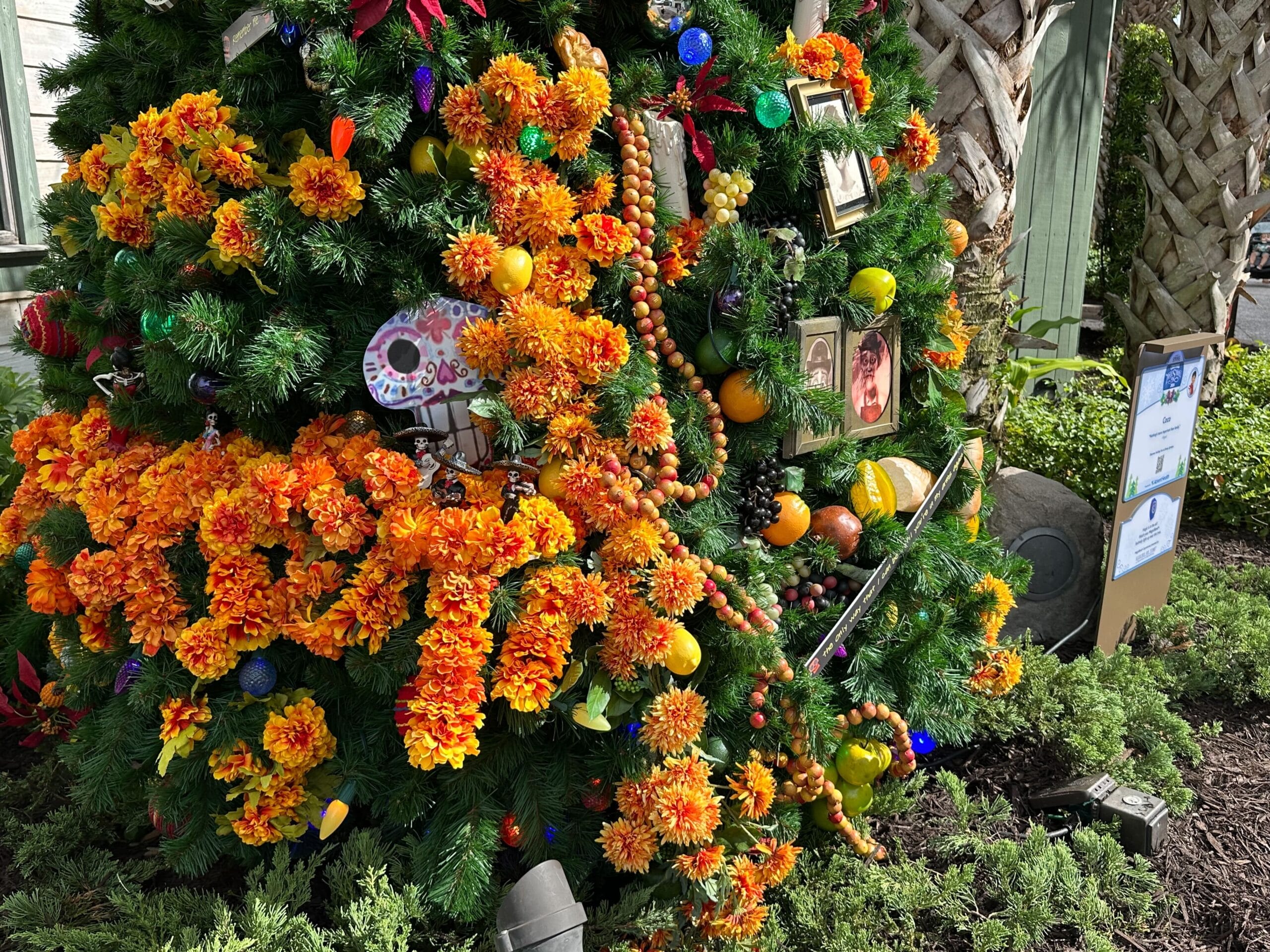 Decorated Christmas tree with vibrant orange flowers, colorful ornaments, and framed photos.