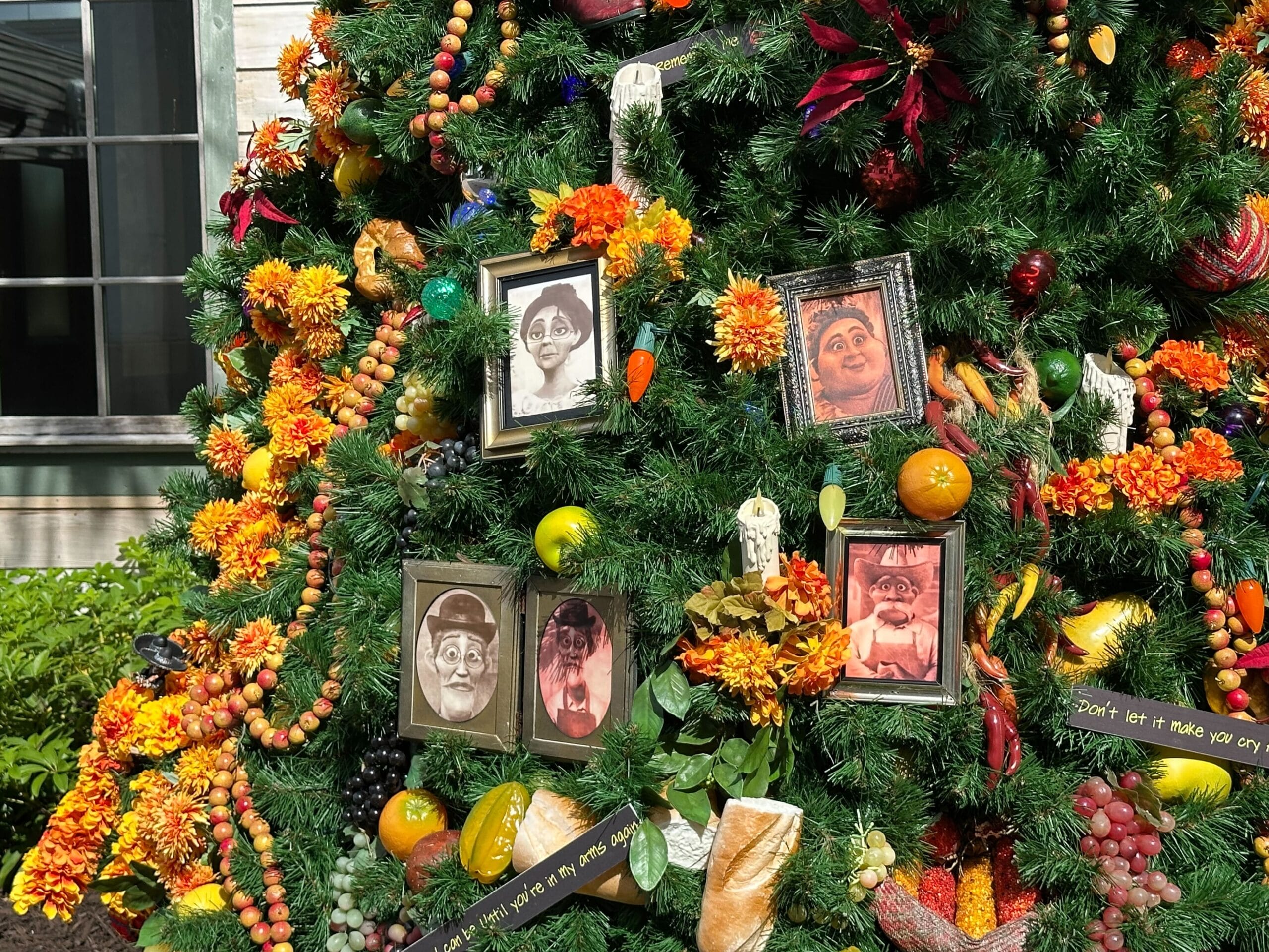 A decorated evergreen with vintage portraits, colorful flowers, fruits, and vegetables. There are several small signs with text and a window visible in the background.